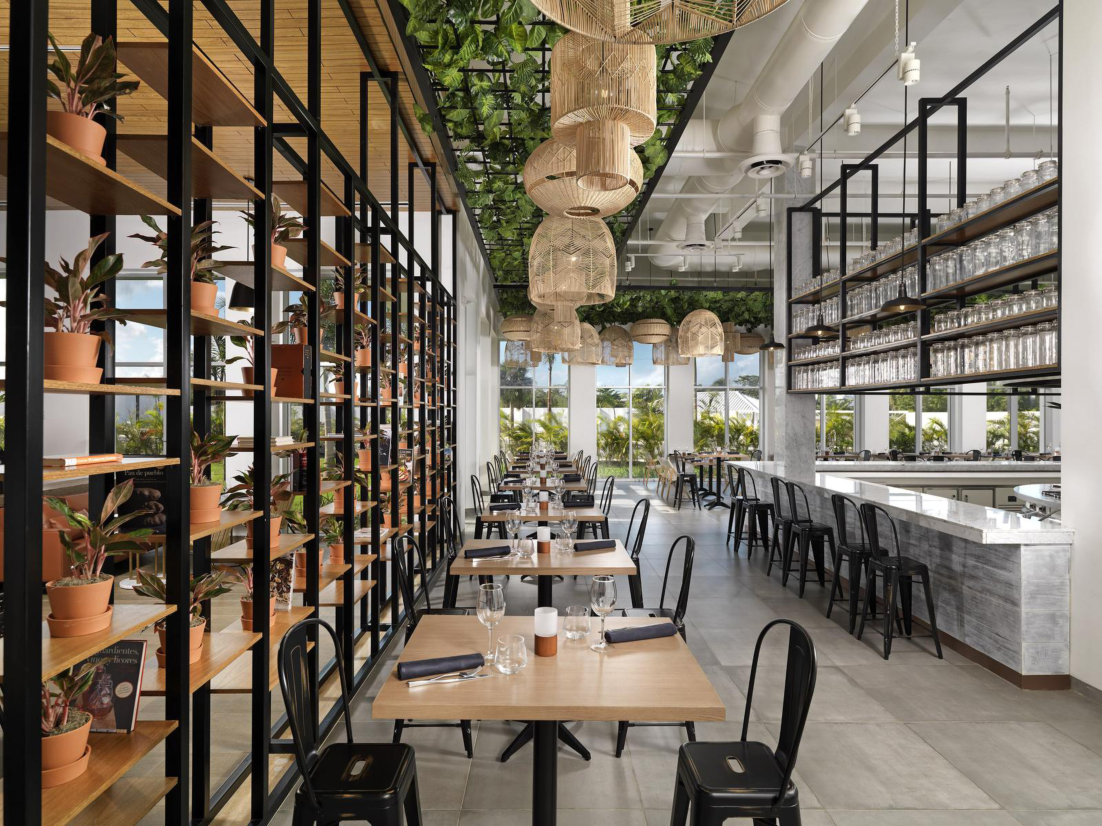 Modern restaurant interior with botanical decor, rattan lighting, and bar.