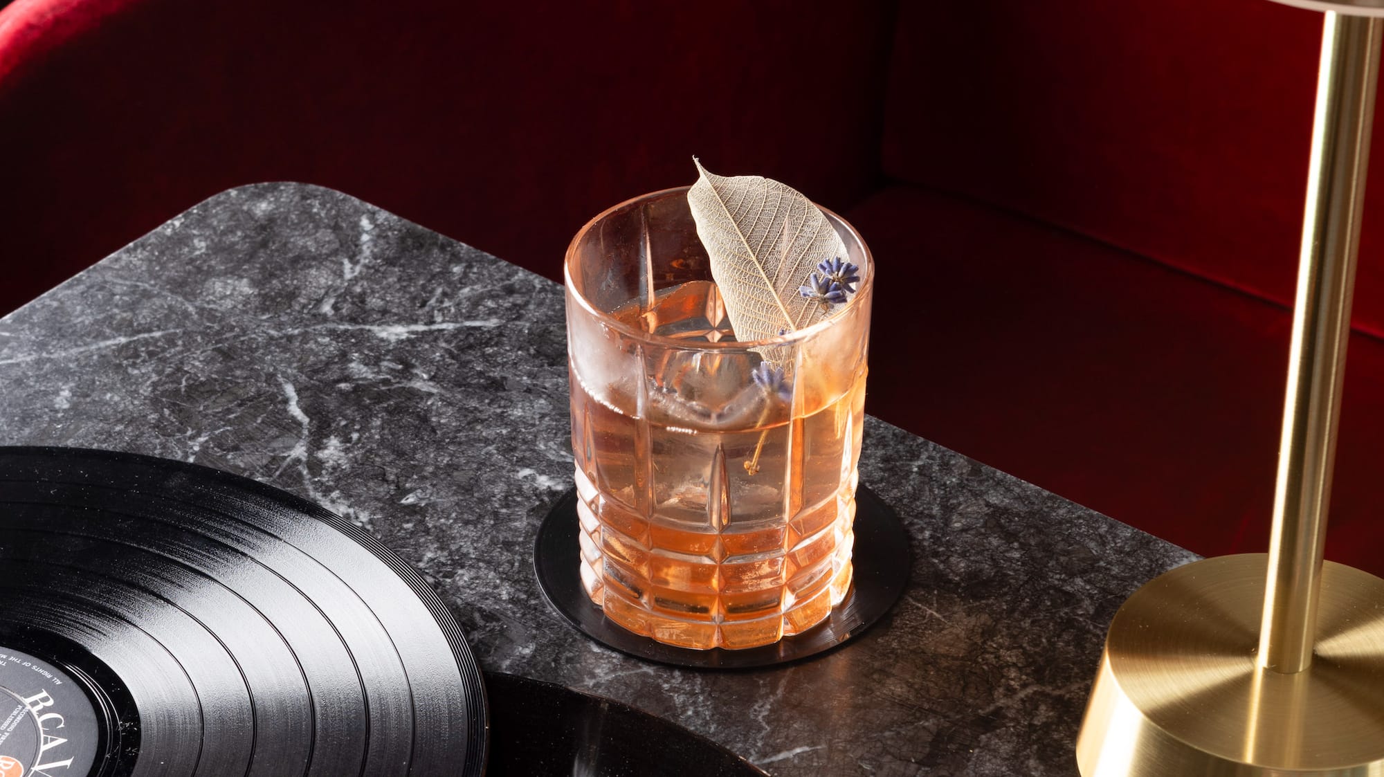 a glass of liquid with a feather on top of a table with vinyl records