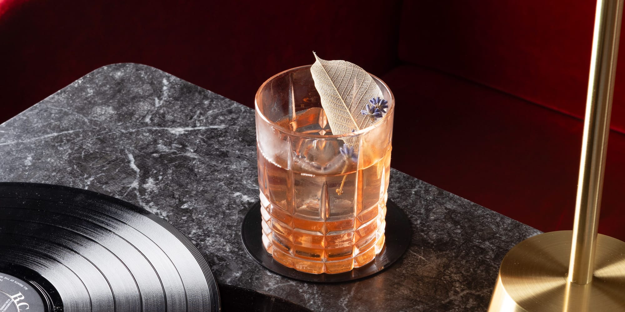 a glass of liquid with a feather on top of a table with vinyl records