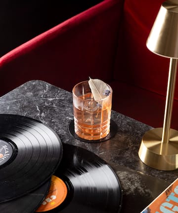 a glass of liquid with a feather on top of a table with vinyl records
