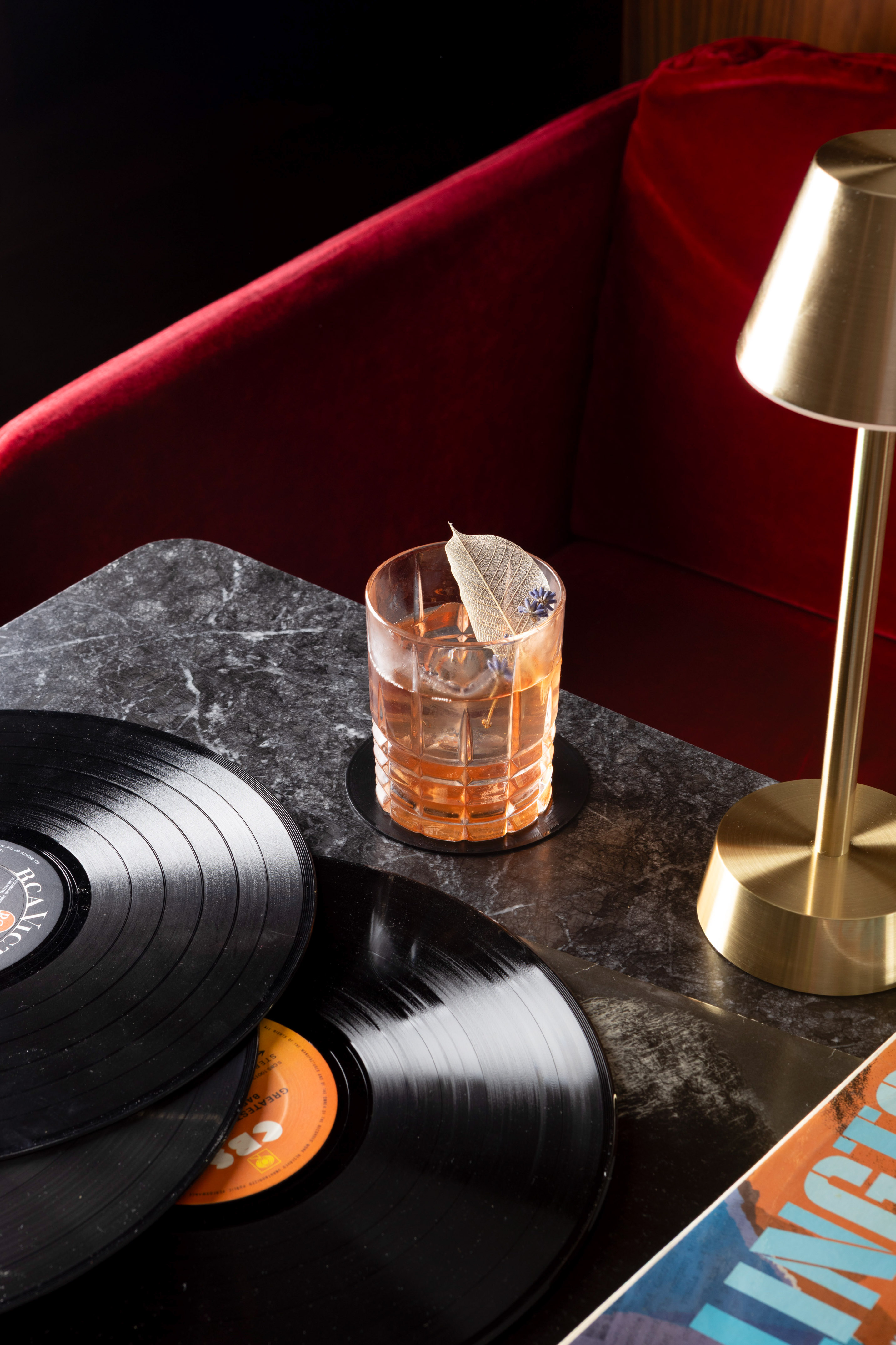 a glass of liquid with a feather on top of a table with vinyl records