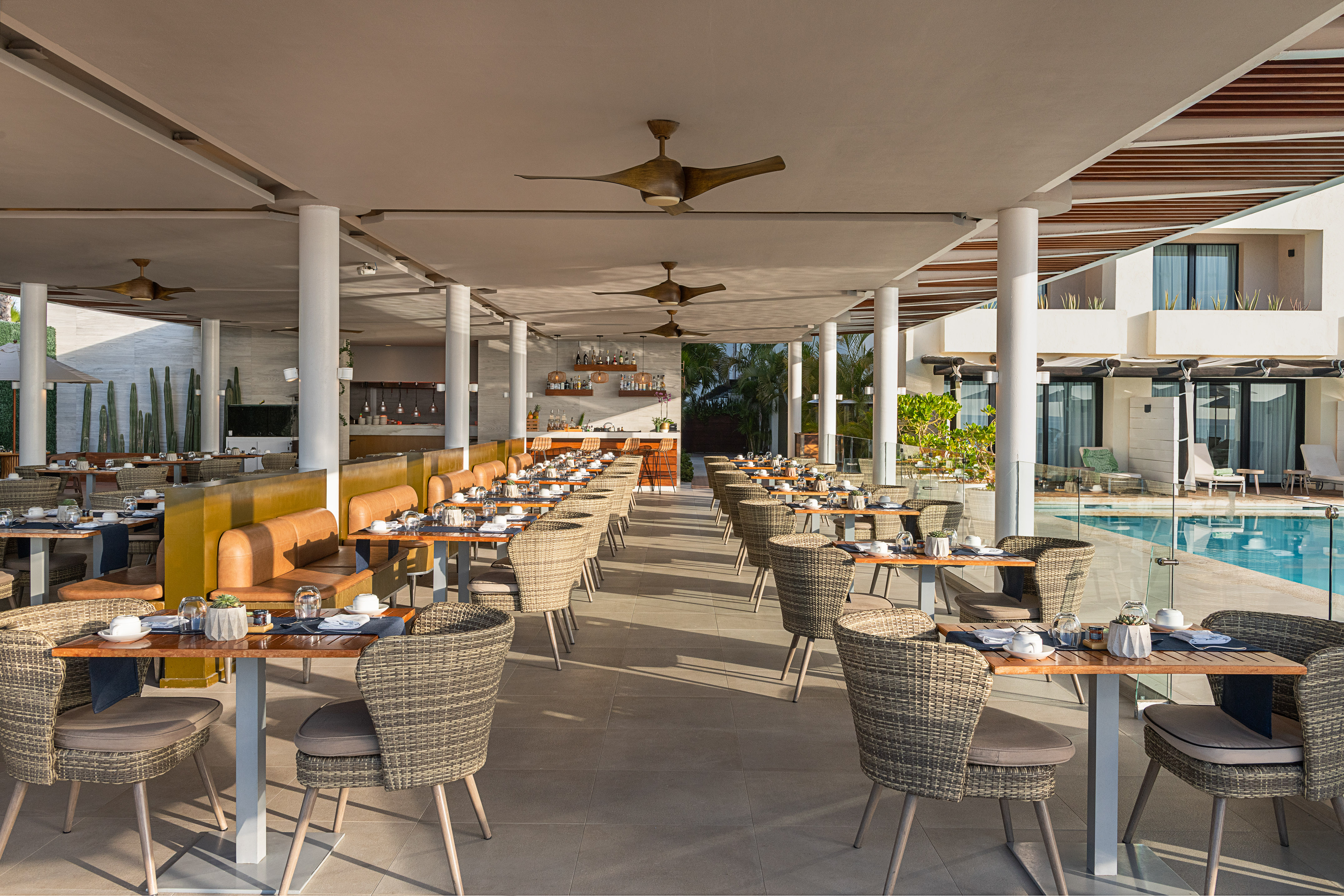 Elegant outdoor resort restaurant with wicker seating, bar, and pool view.