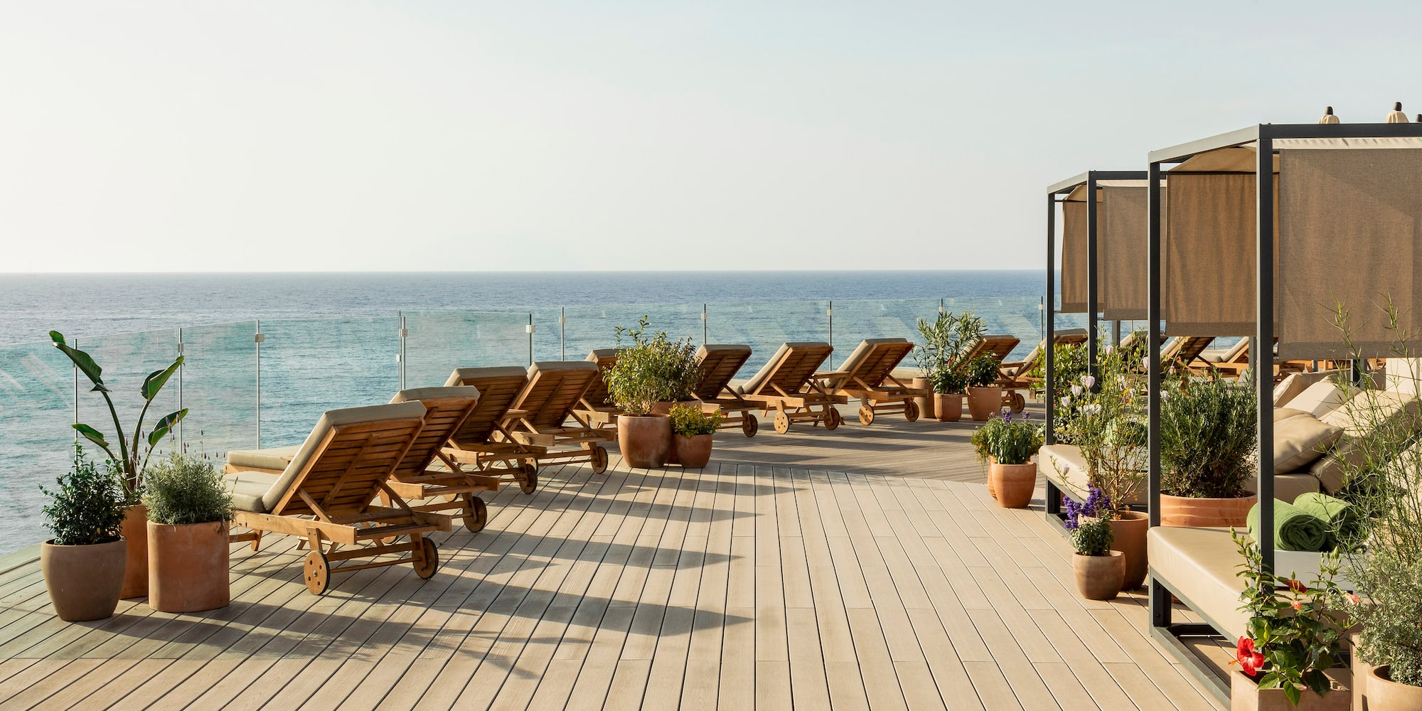Rooftop terrace with ocean view, wooden lounge chairs, and daybed cabanas.