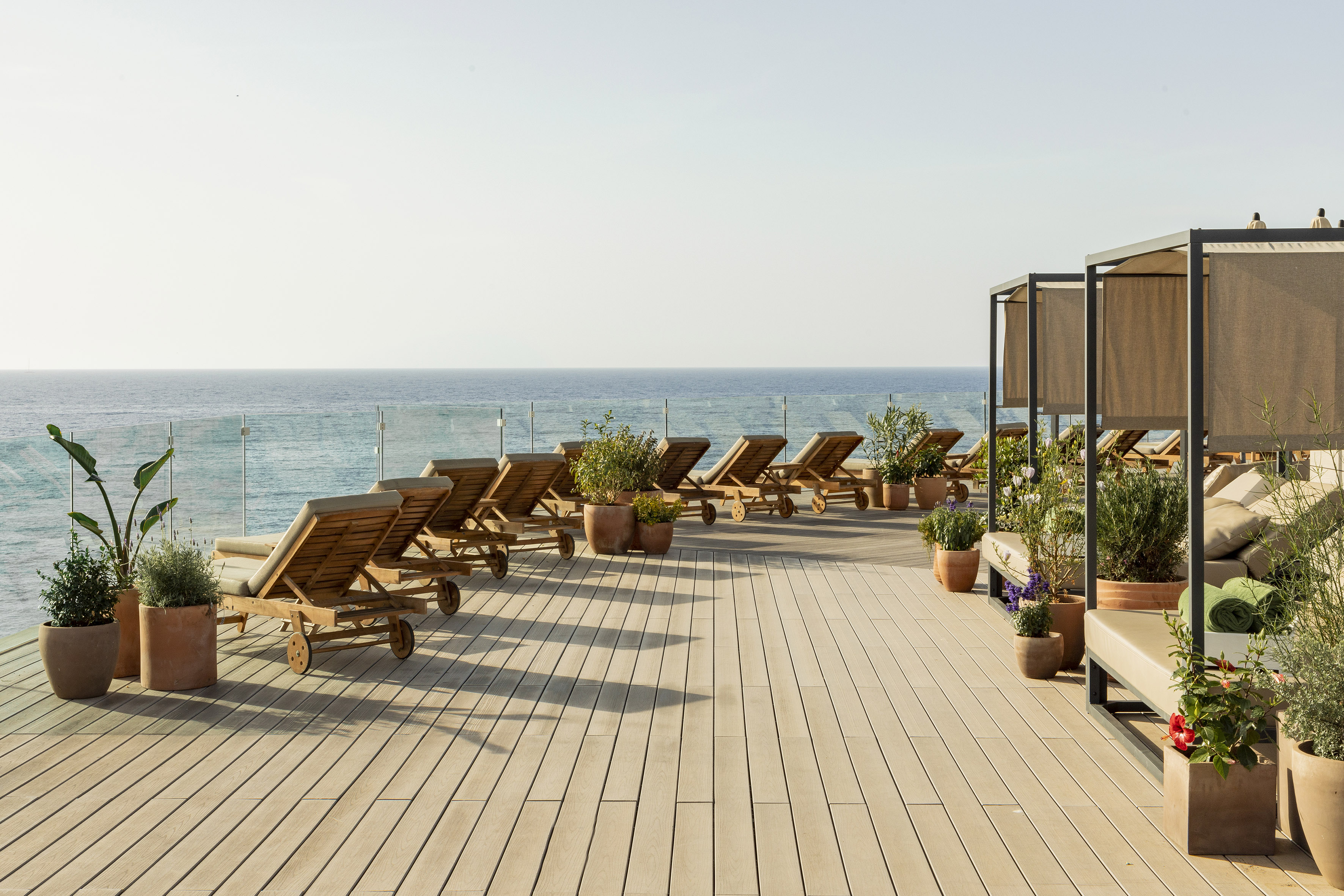 Rooftop terrace with ocean view, wooden lounge chairs, and daybed cabanas.
