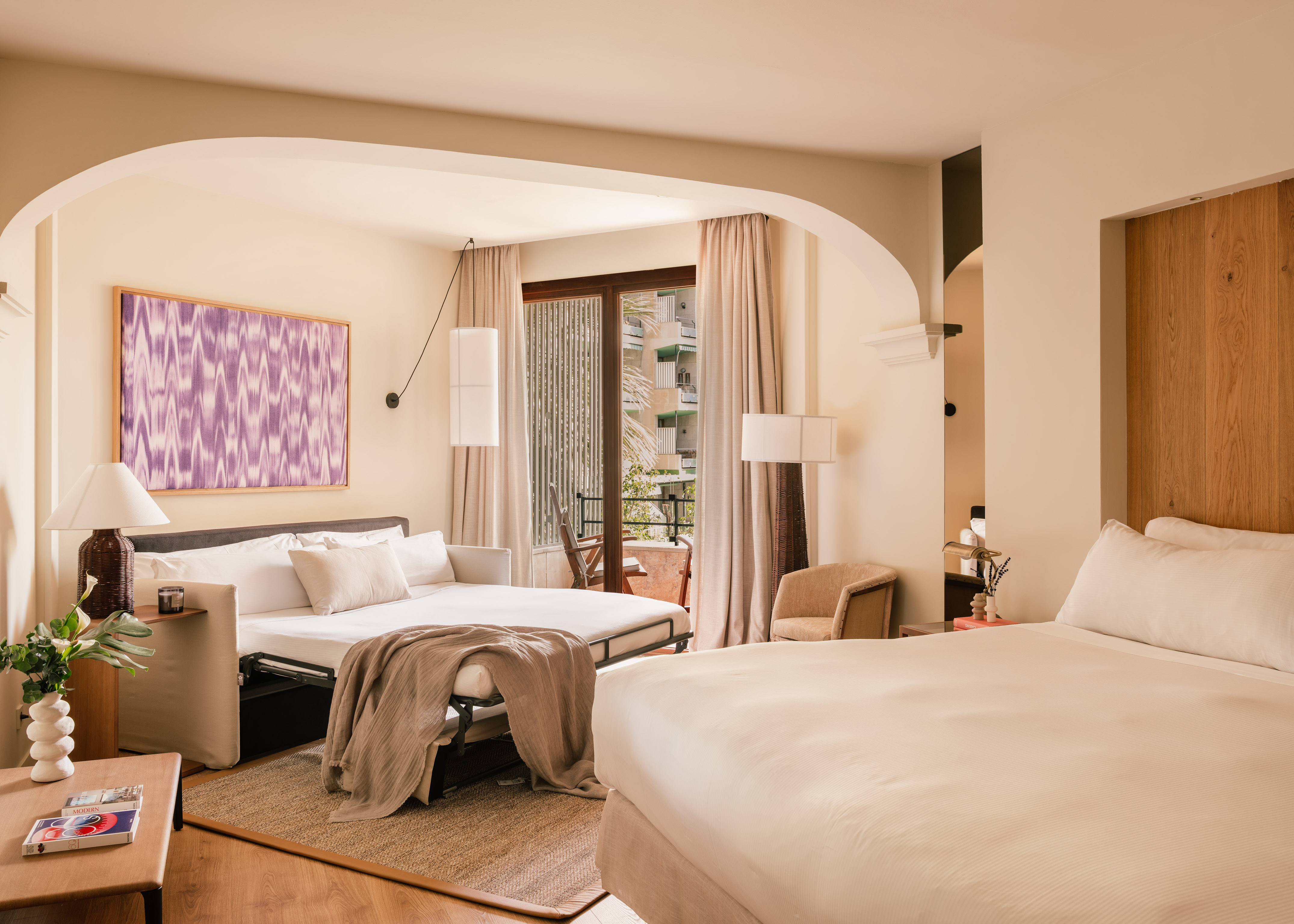Spacious hotel suite with main bed, sofa bed, and private balcony.