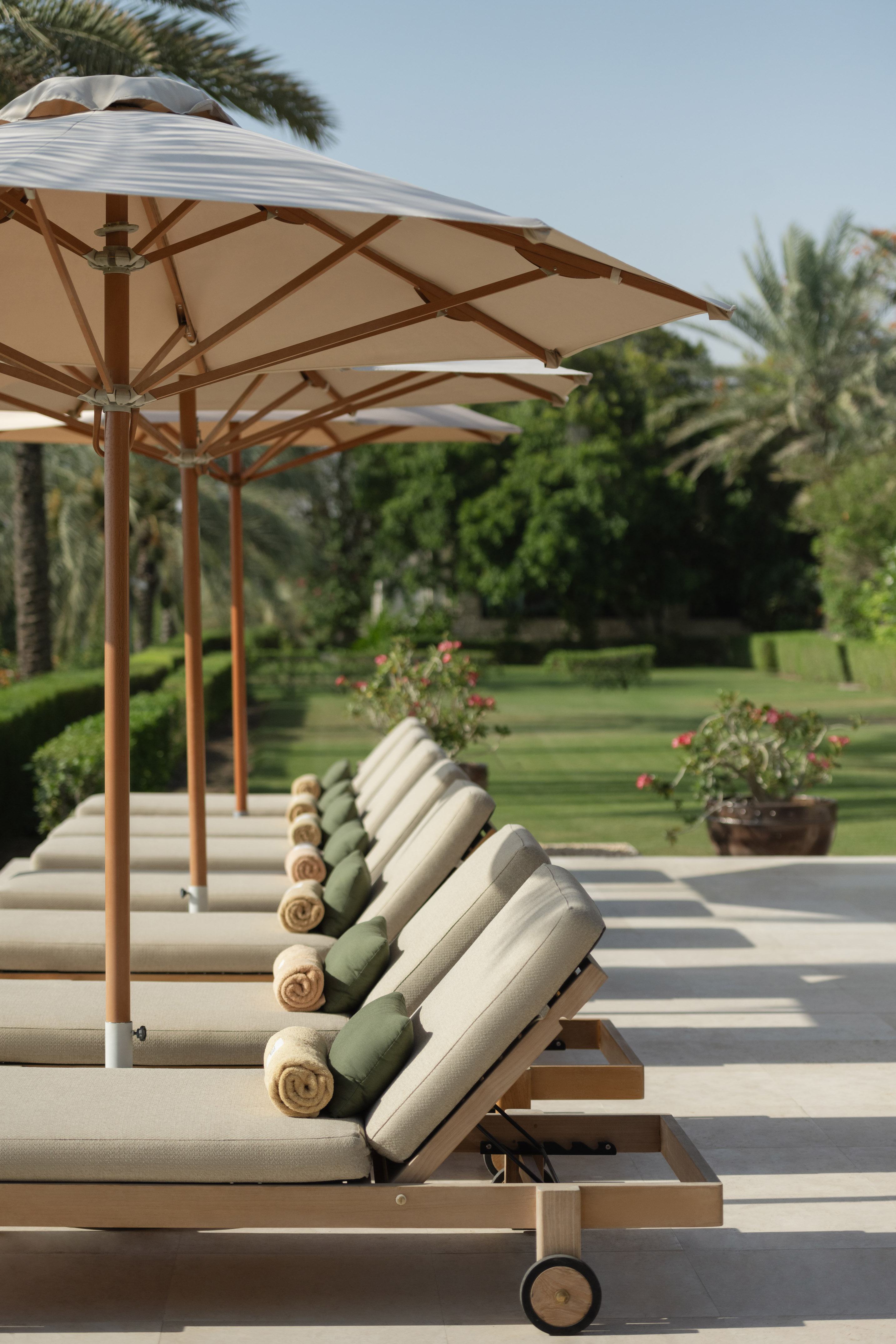 Sun loungers with umbrellas line a resort patio beside a green garden.