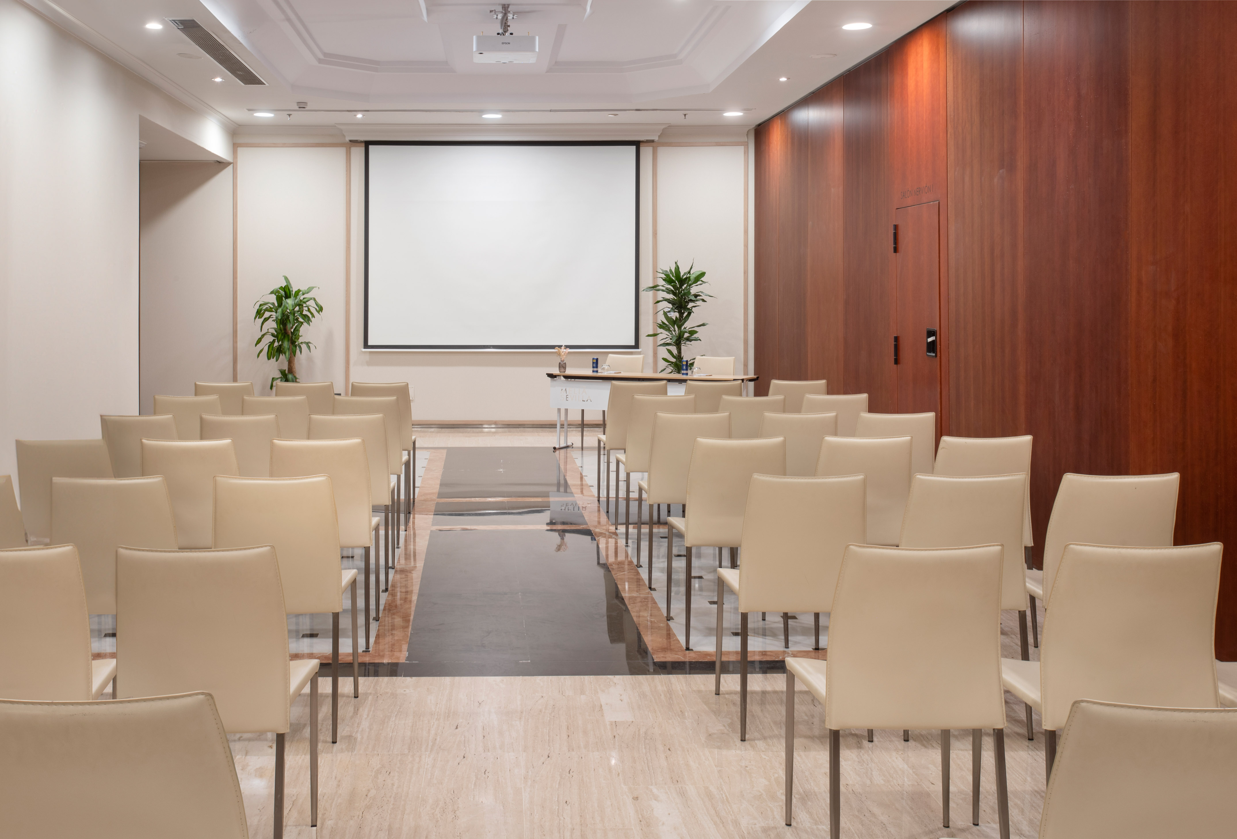 Empty conference room setup with projector screen and rows of beige chairs.