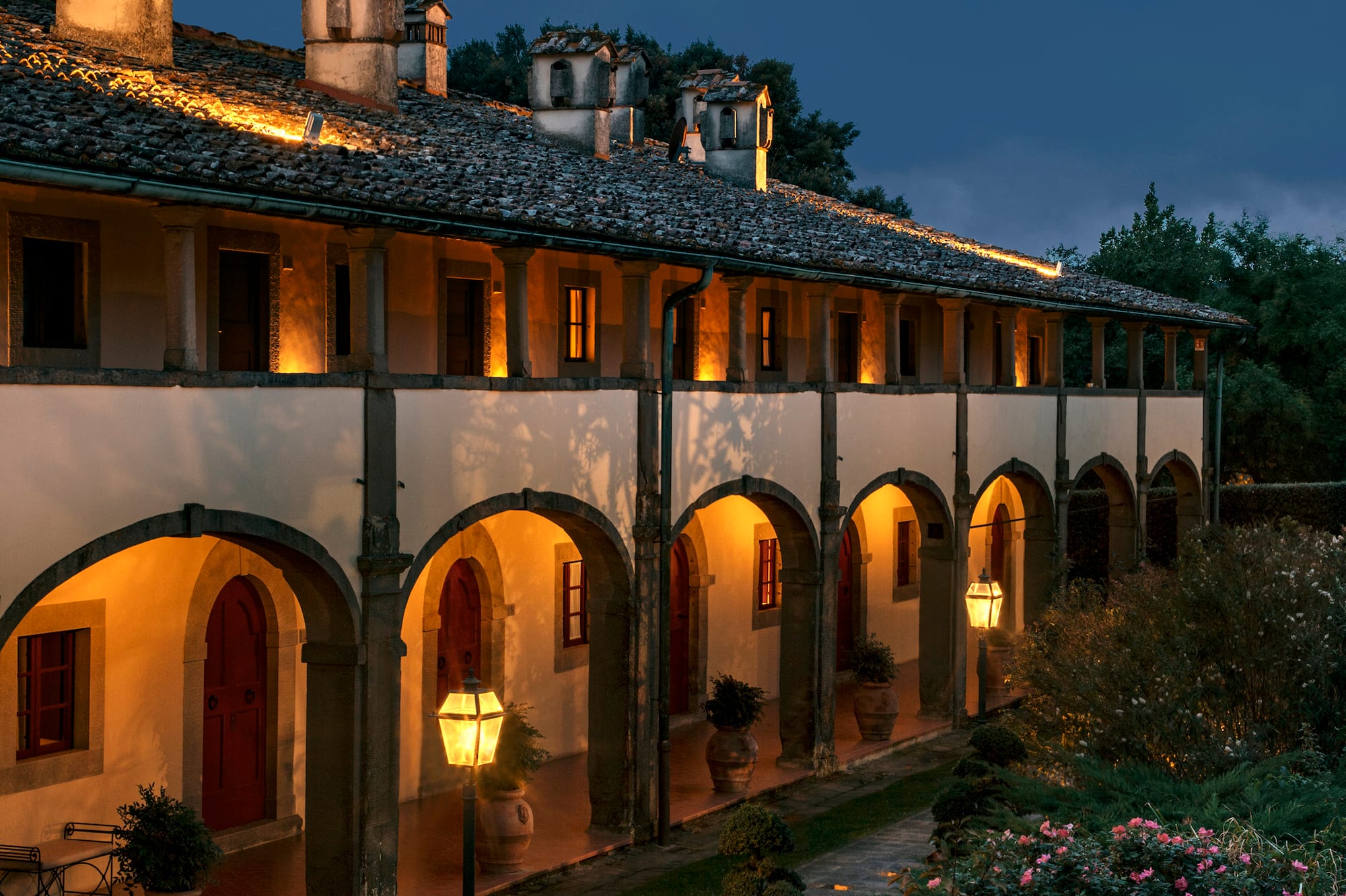 Traditional arched building illuminated at dusk, with lush garden and path.