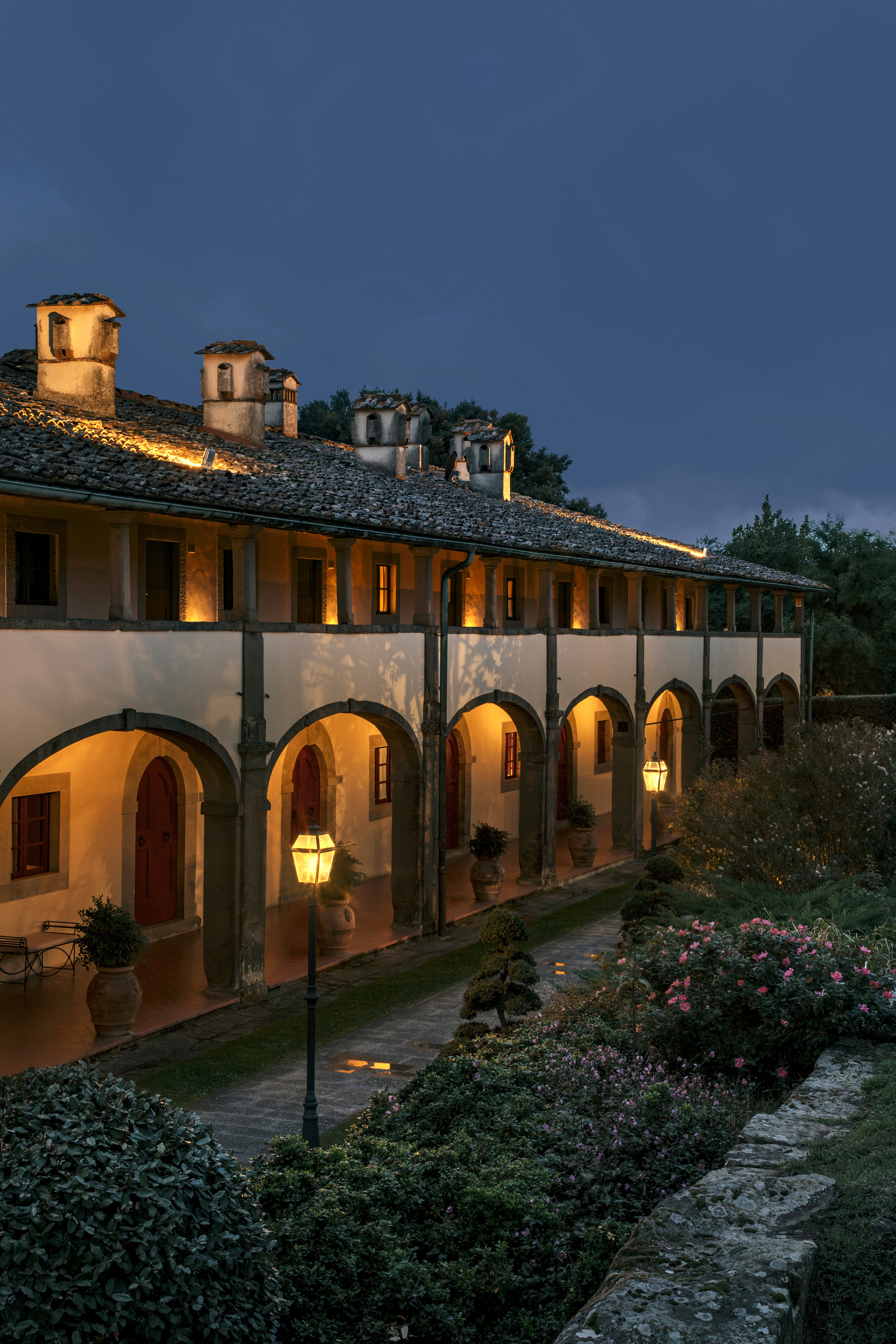 Traditional arched building illuminated at dusk, with lush garden and path.