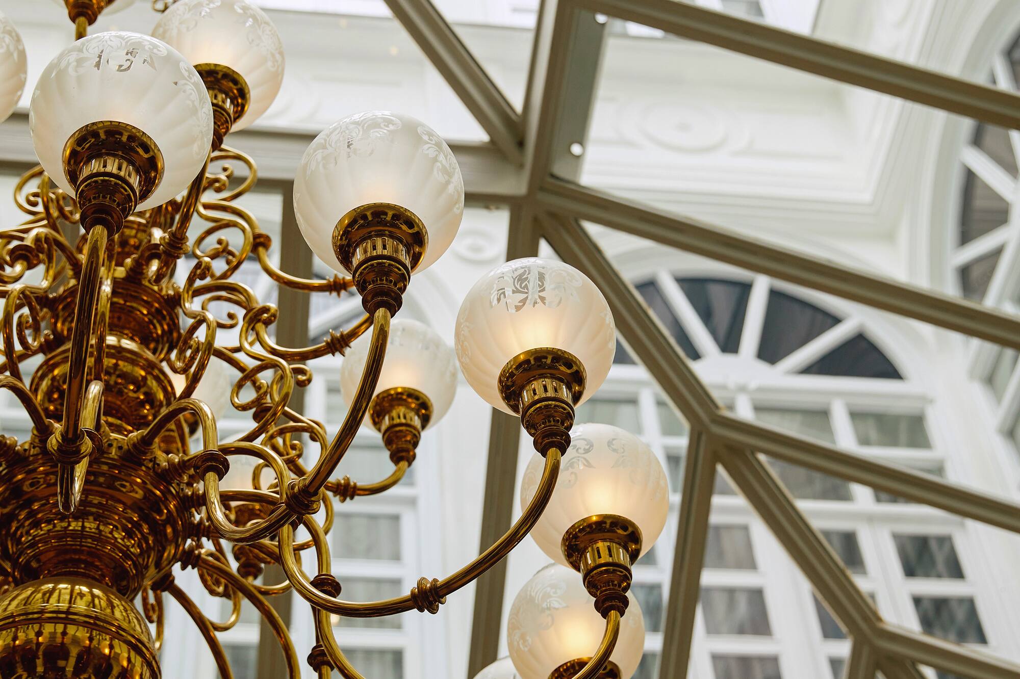 Ornate brass chandelier with frosted glass globes under a glass atrium ceiling.