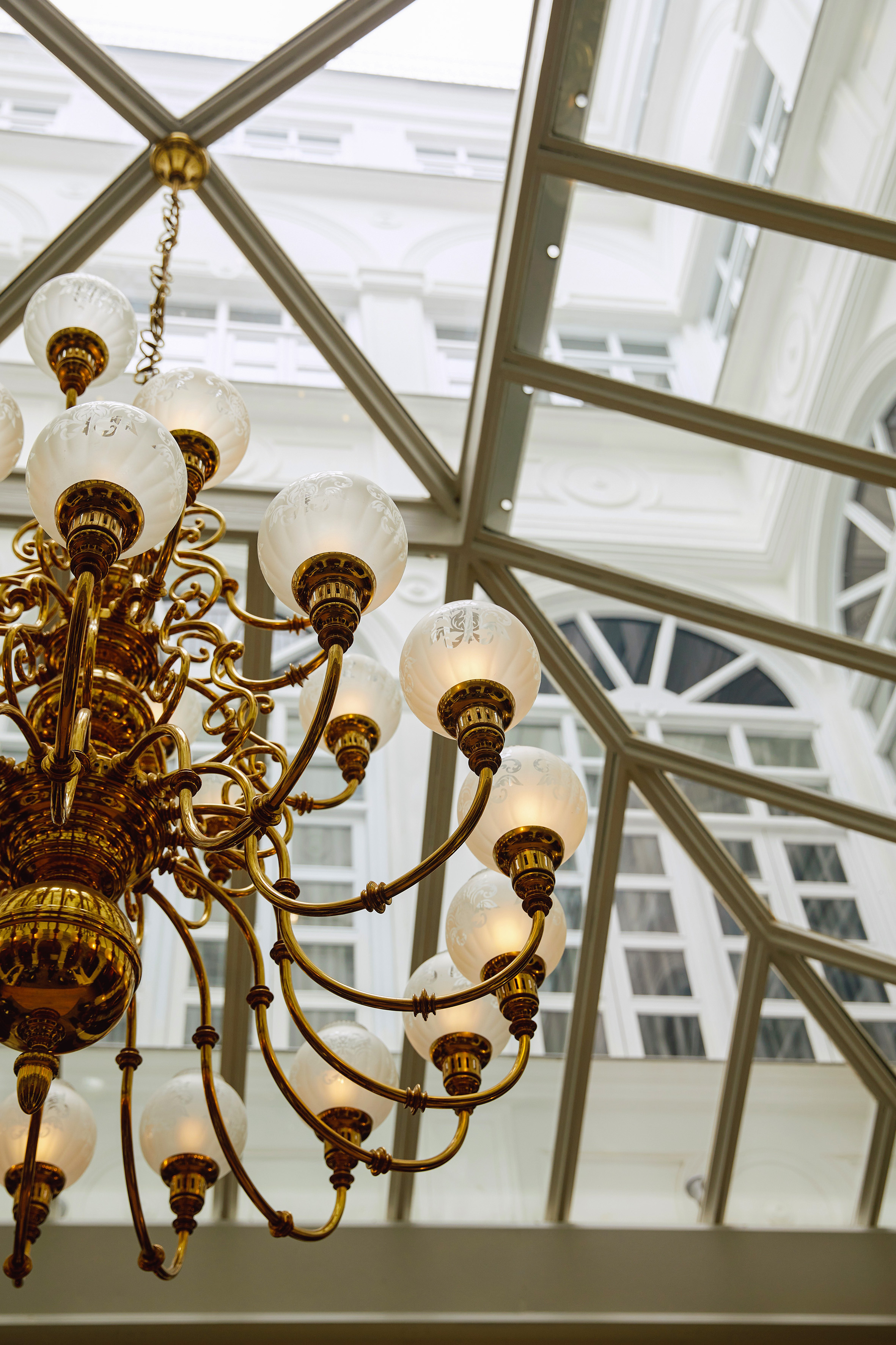 Ornate brass chandelier with frosted glass globes under a glass atrium ceiling.