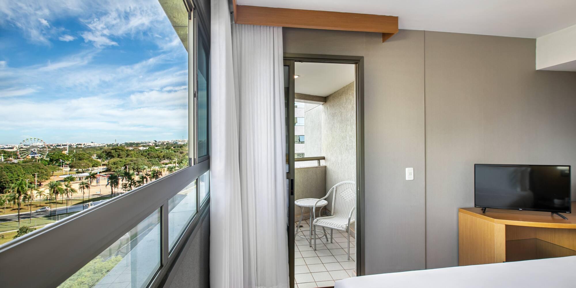 Hotel room with panoramic city view, balcony, and distant Ferris wheel.