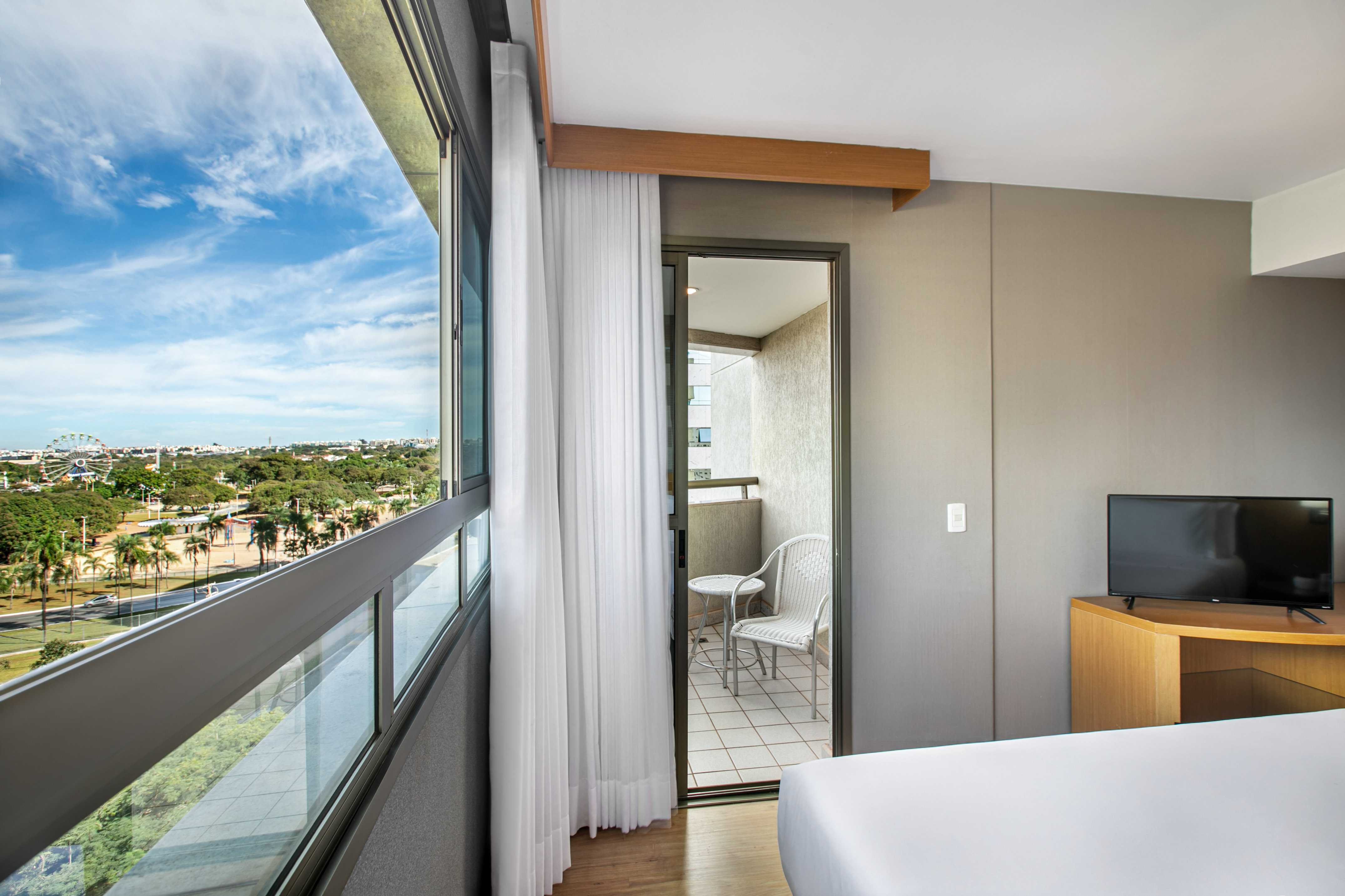 Hotel room with panoramic city view, balcony, and distant Ferris wheel.