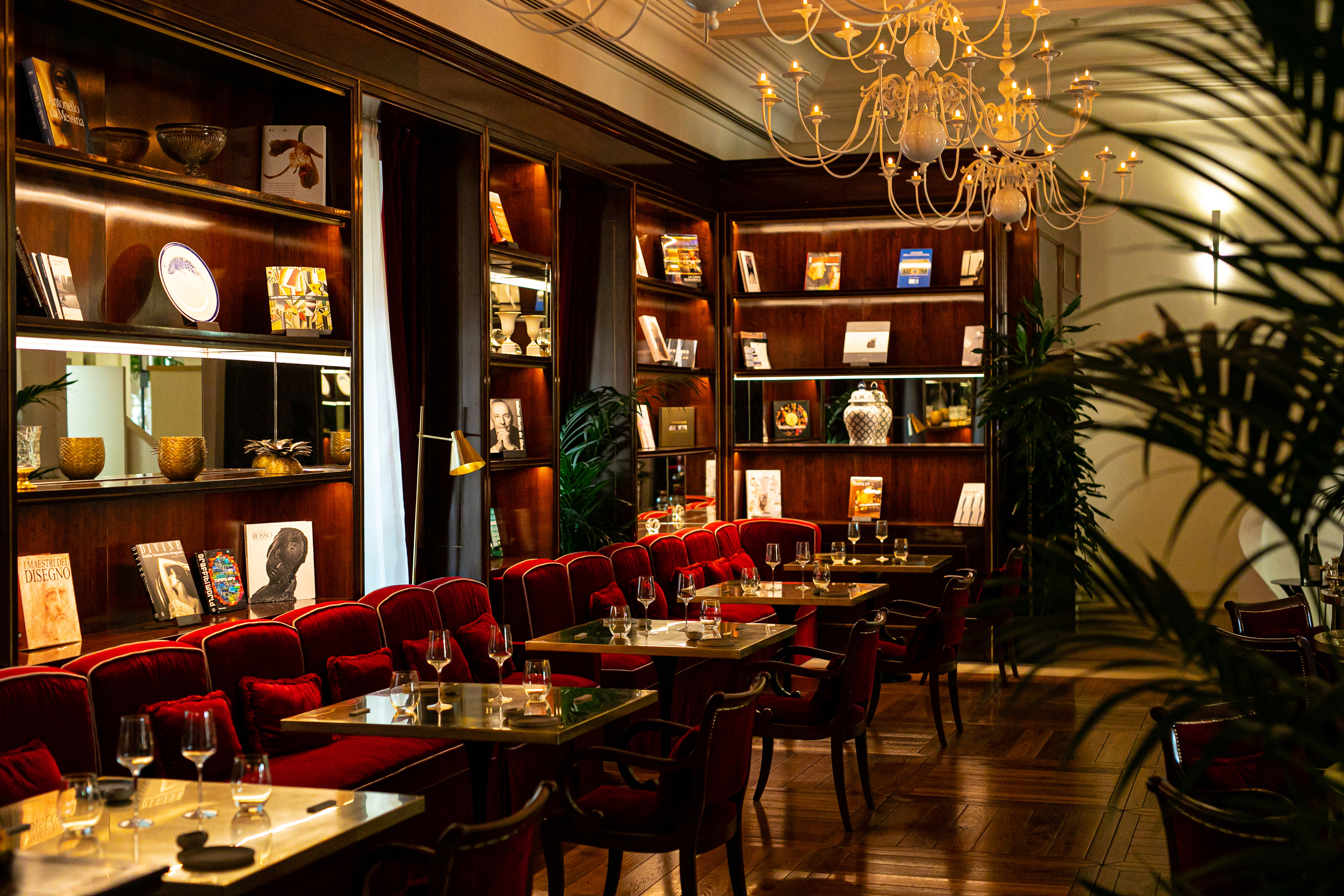 Luxury restaurant with red velvet seating, dark wood library, and chandelier.