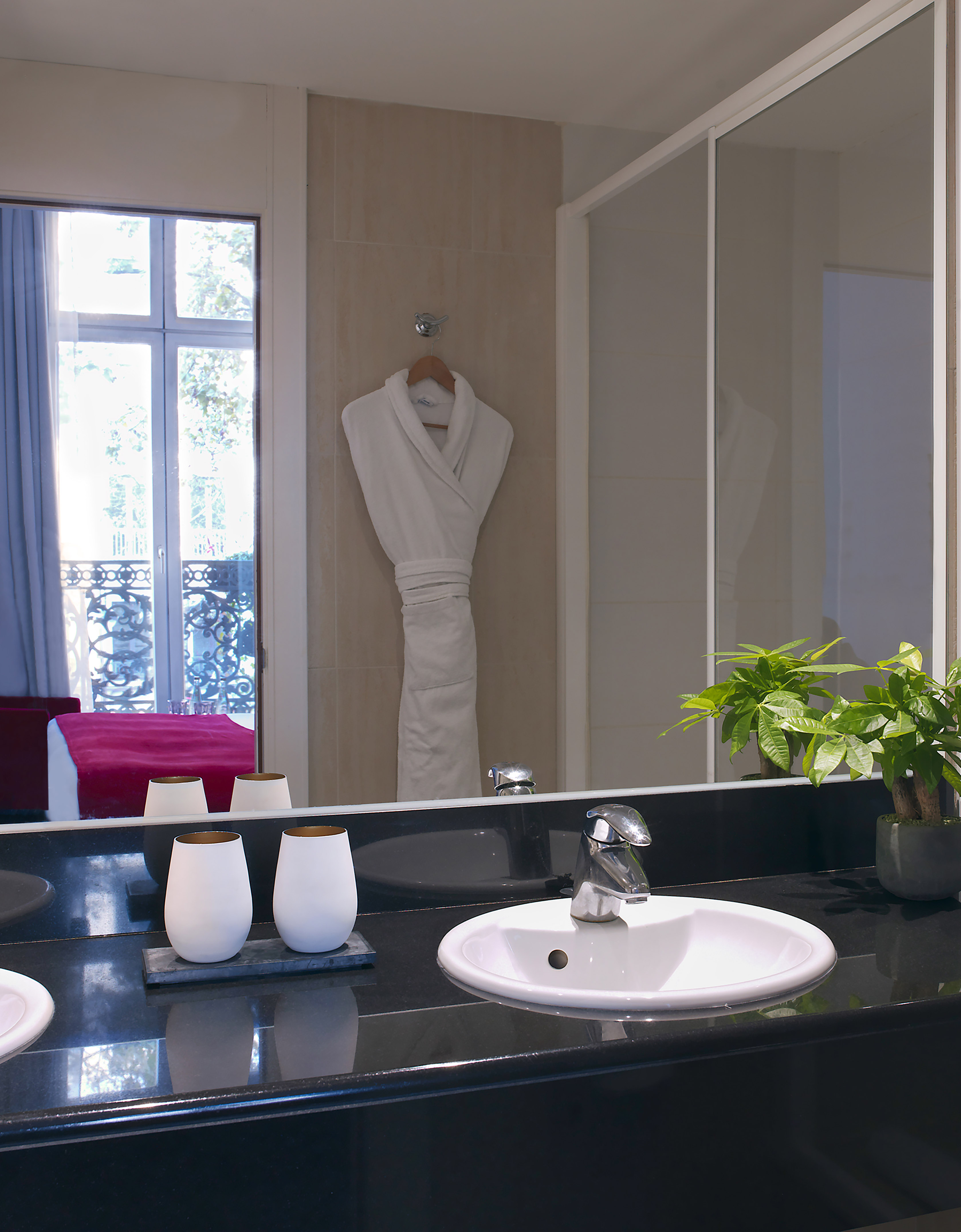 Modern hotel bathroom vanity with sink, mirror reflecting window, and bathrobe.