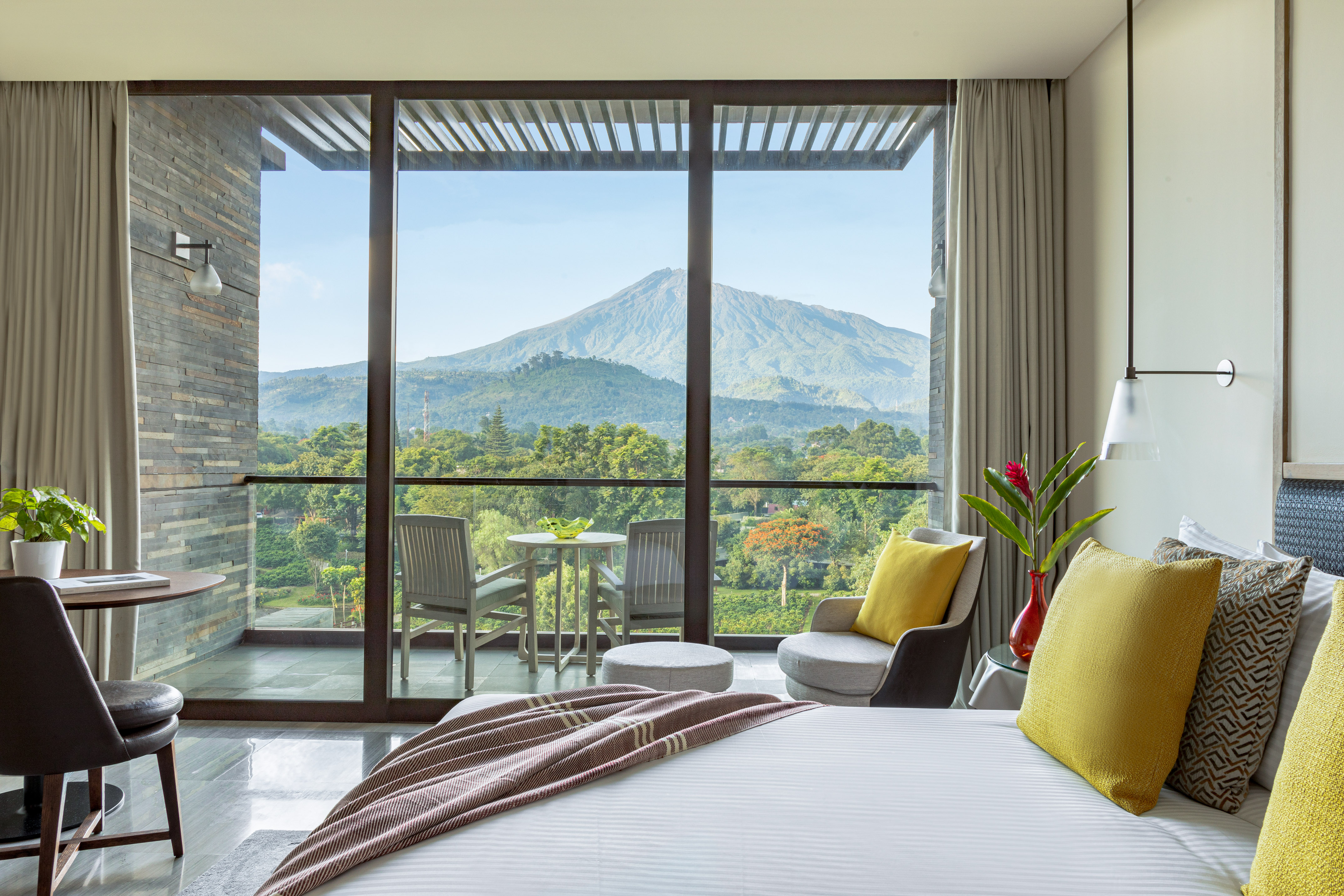 Modern hotel room with balcony, lush mountain view, and contemporary design.