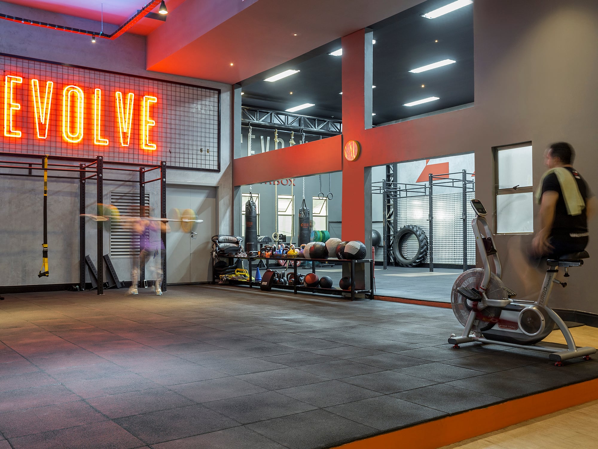 Modern Evolve gym with neon sign, fitness equipment, and exercising people.