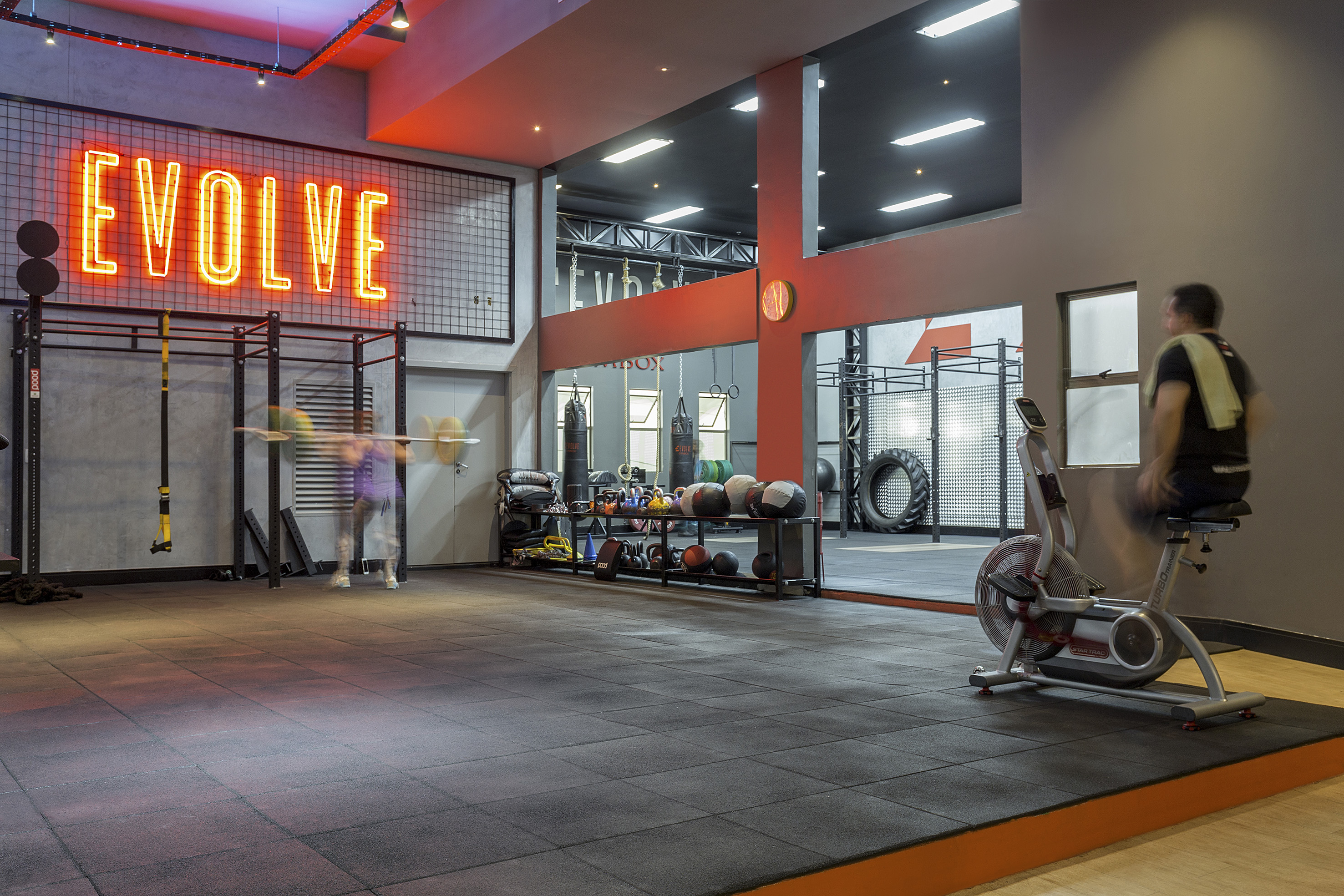 Modern Evolve gym with neon sign, fitness equipment, and exercising people.