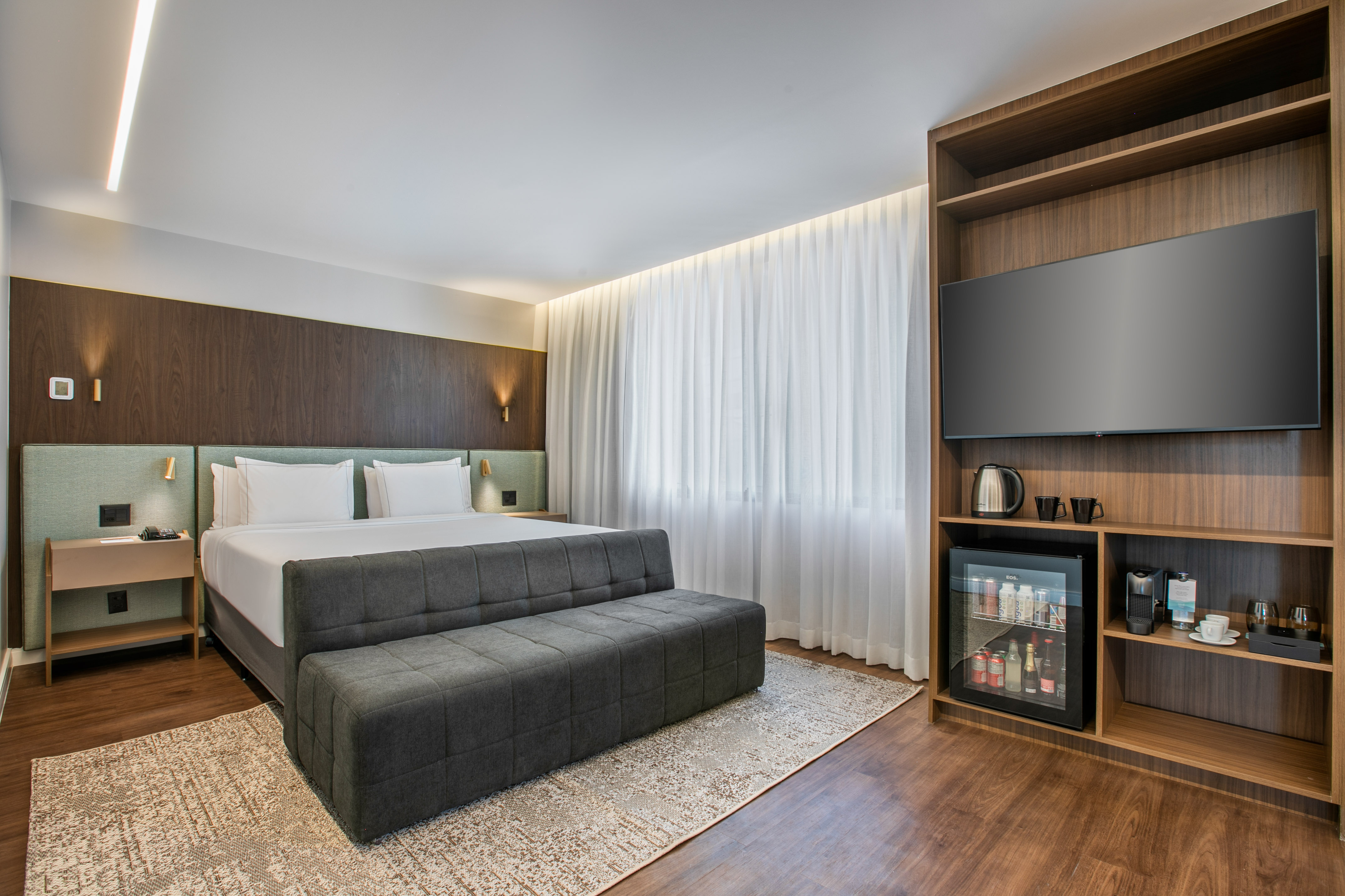 Stylish hotel bedroom with queen bed, smart TV, and stocked mini-fridge.