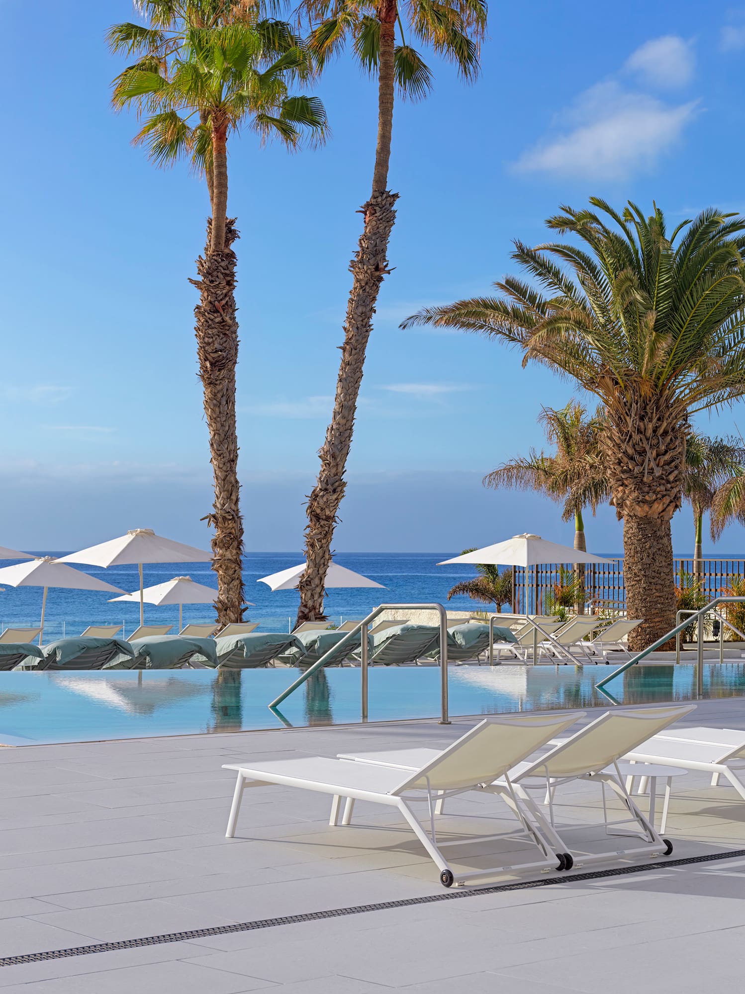 a pool with lounge chairs and umbrellas by the ocean