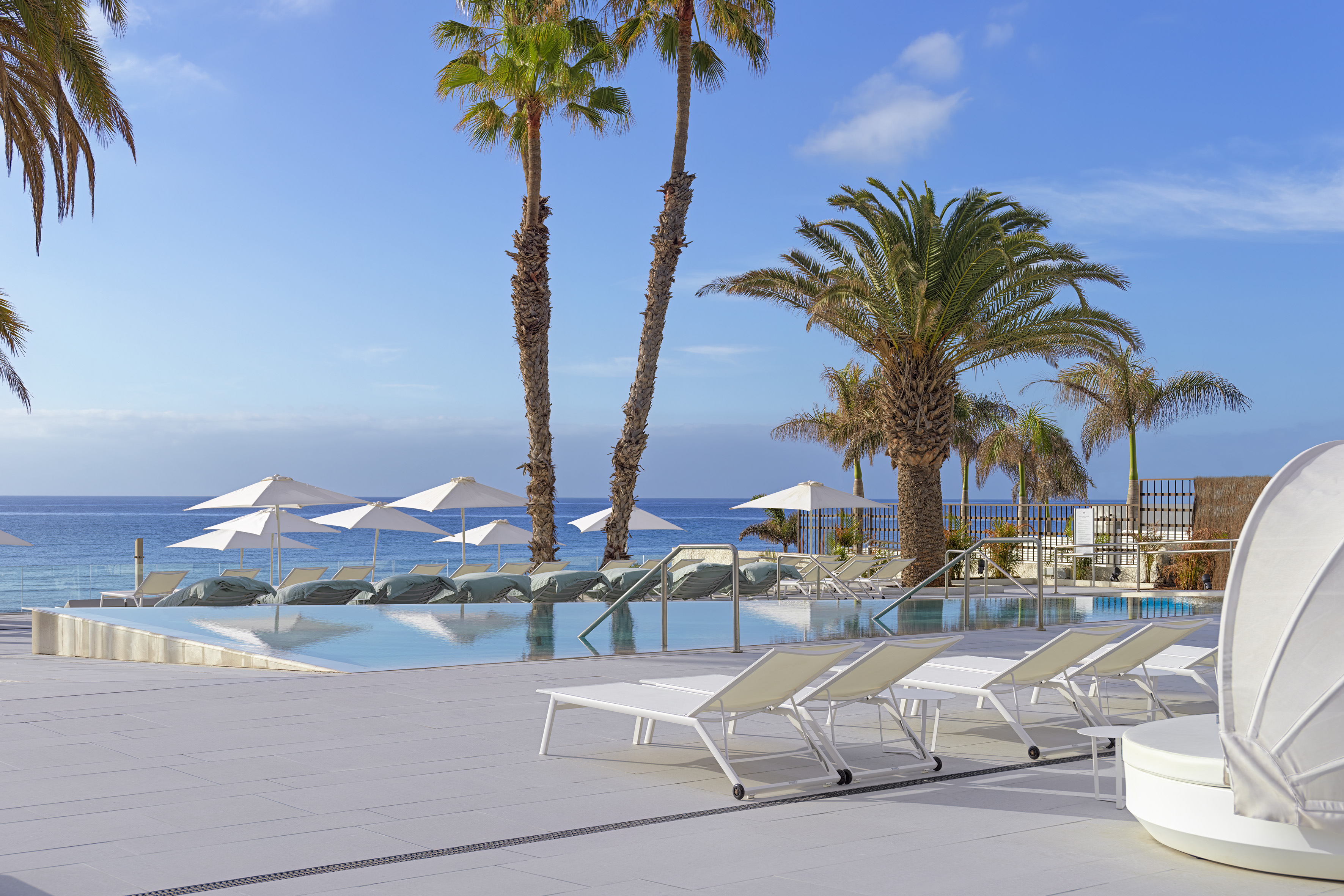 a pool with lounge chairs and umbrellas by the ocean