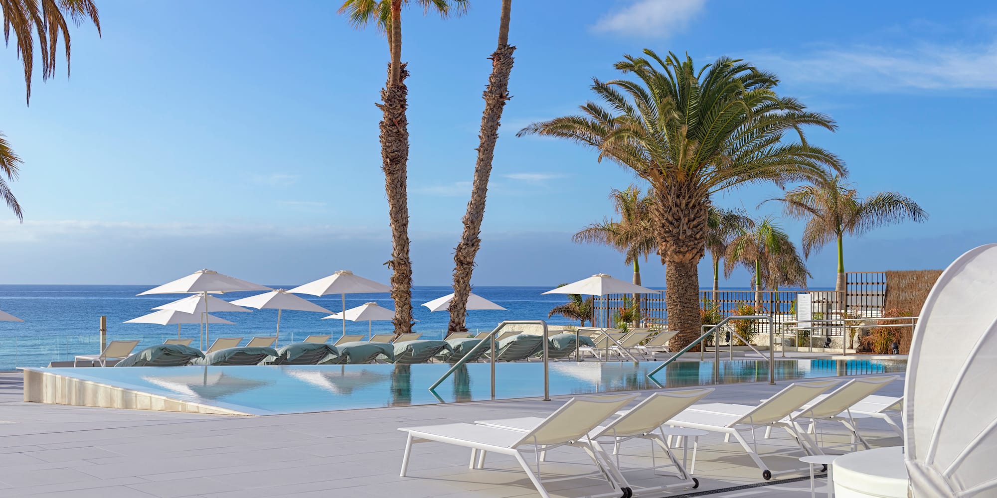a pool with lounge chairs and umbrellas by the ocean