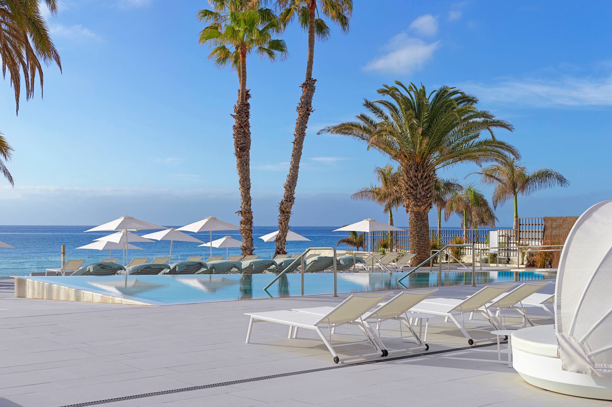 a pool with lounge chairs and umbrellas by the ocean