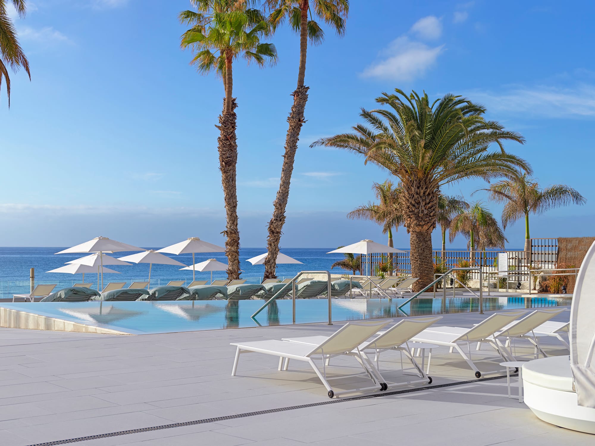 a pool with lounge chairs and umbrellas by the ocean