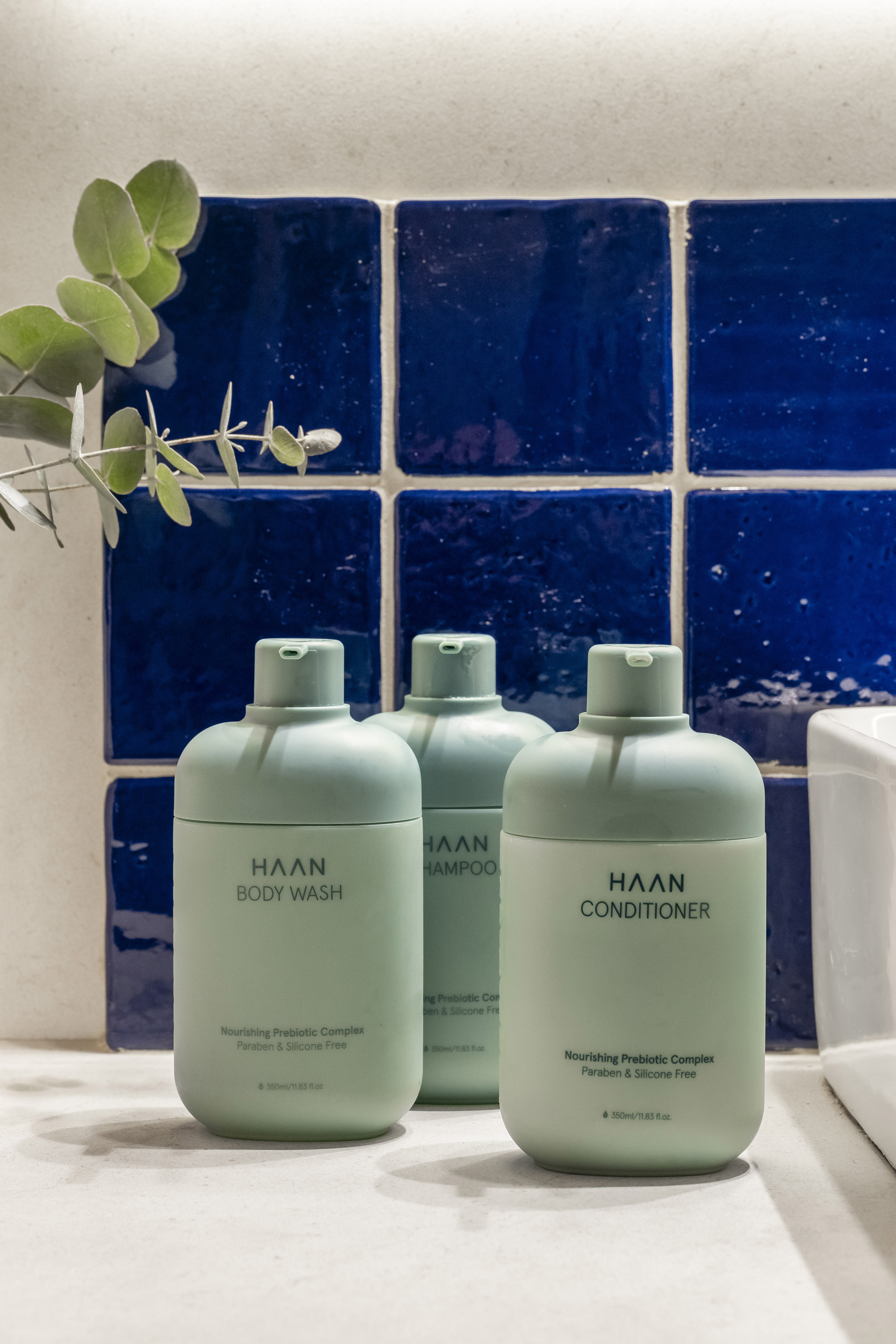 HAAN body wash, shampoo, and conditioner bottles with eucalyptus against blue tiles.