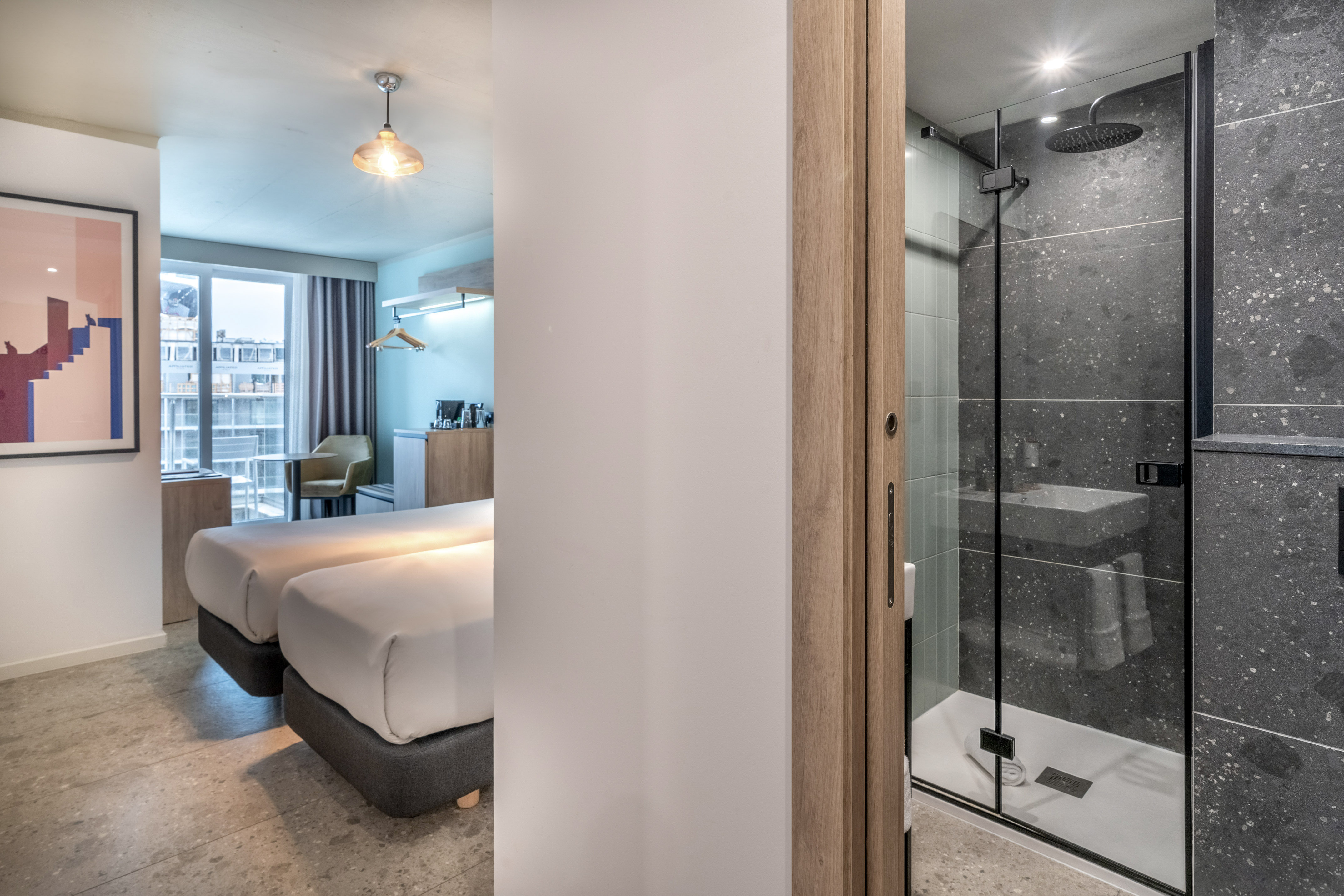 Modern hotel room with twin beds and a dark-tiled, walk-in shower.