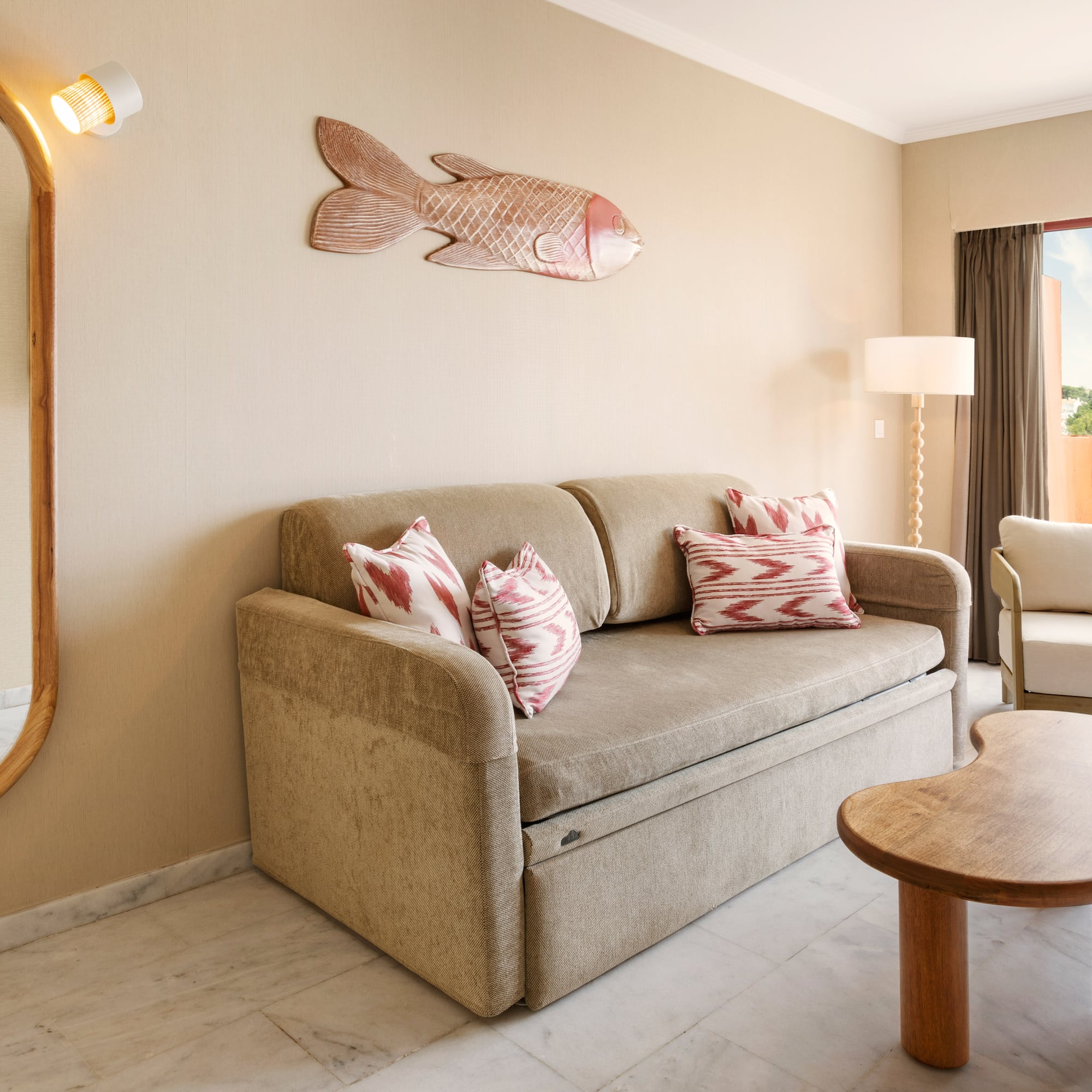 Hotel suite living room with sofa bed, balcony, and tropical fish decor.