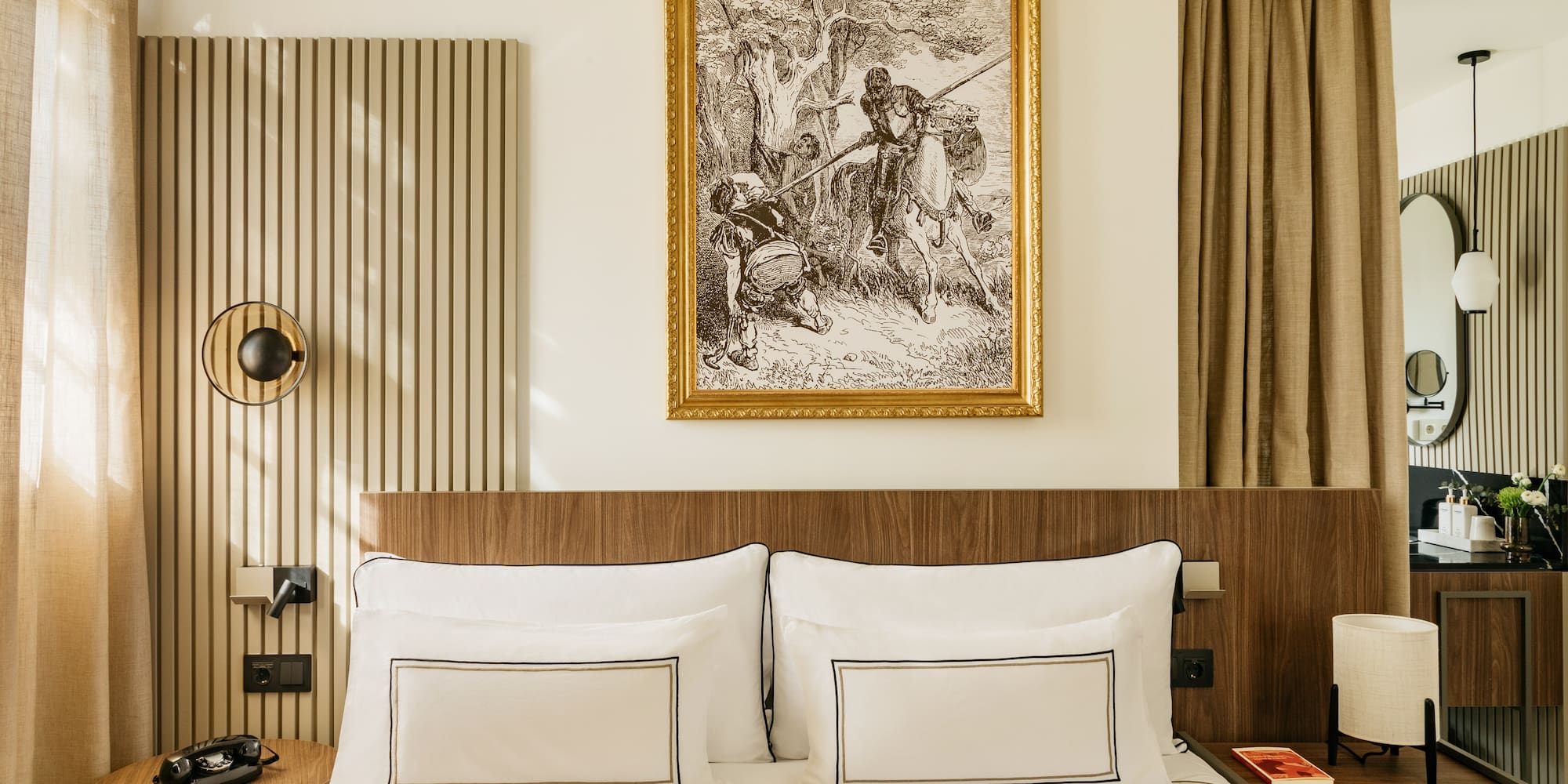 Modern hotel bedroom with wooden headboard, elegant white bed, and framed classic art.
