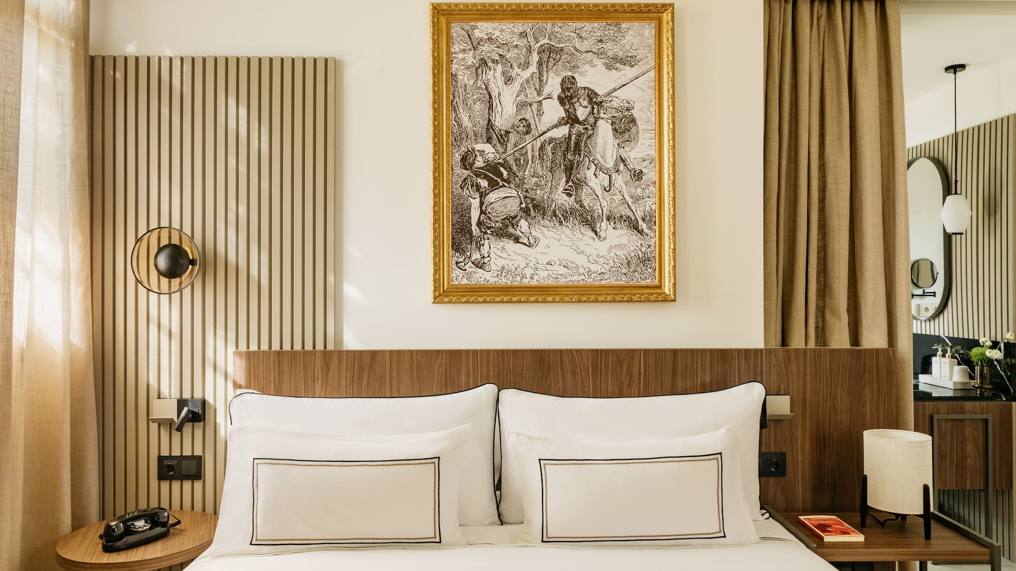 Modern hotel bedroom with wooden headboard, elegant white bed, and framed classic art.
