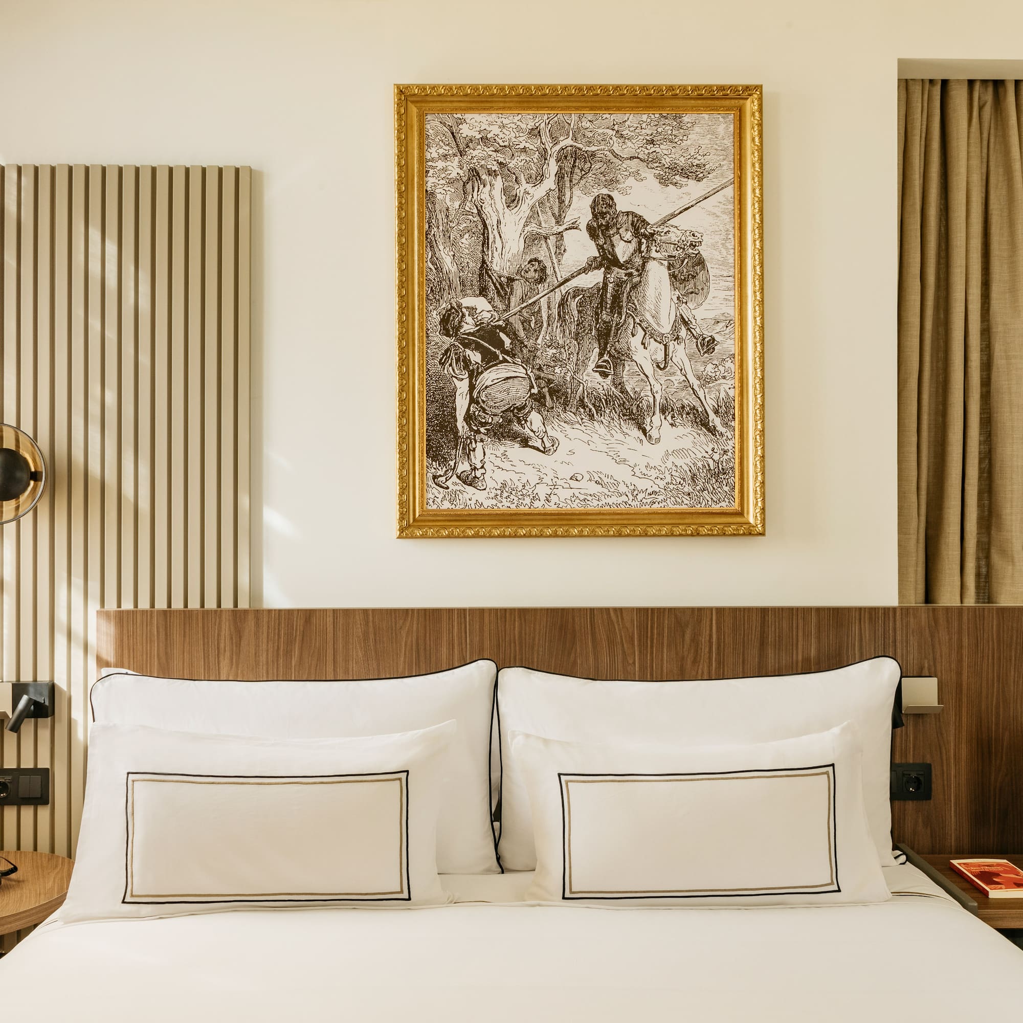 Modern hotel bedroom with wooden headboard, elegant white bed, and framed classic art.