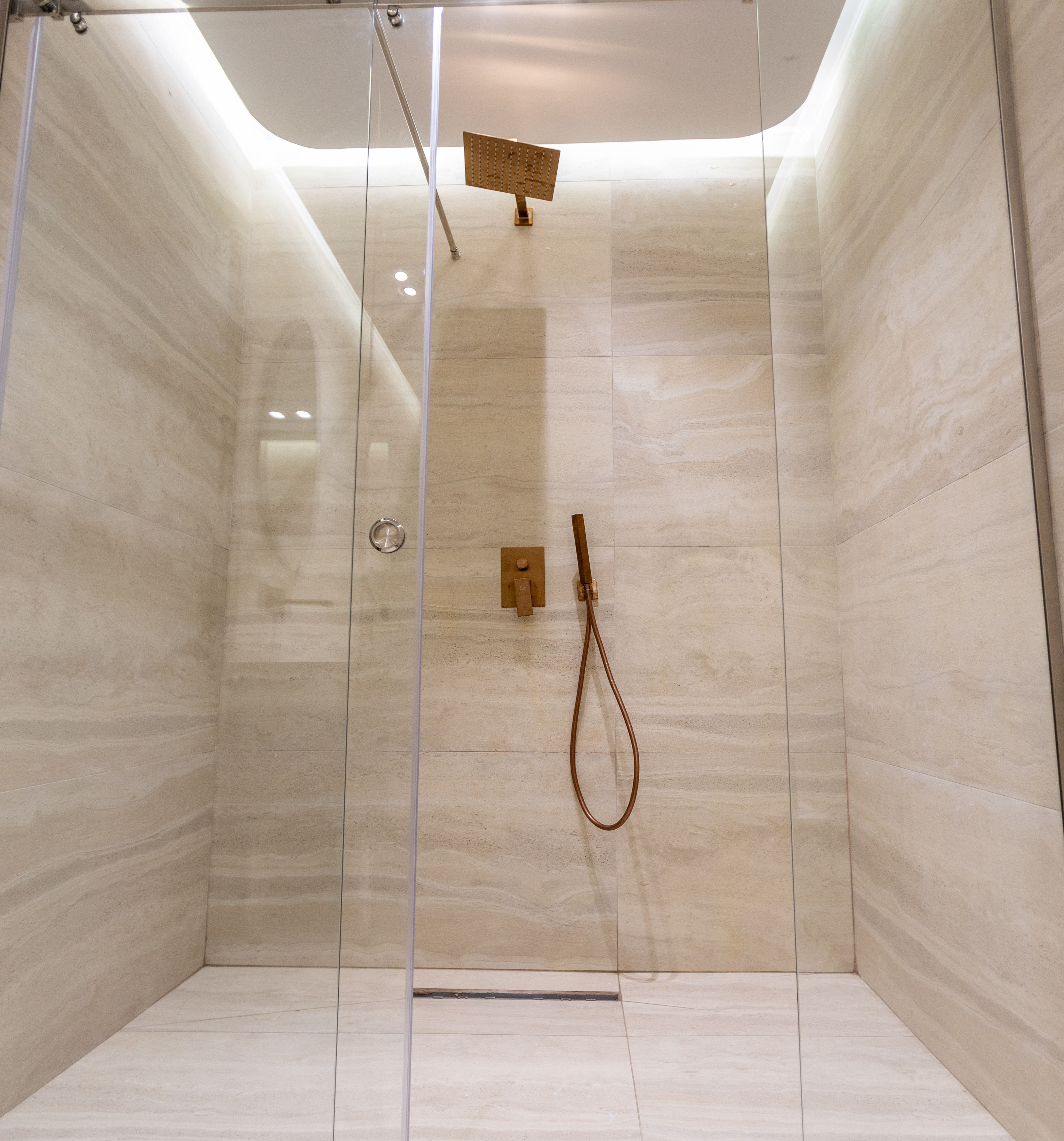 Beige tiled modern shower with glass enclosure, bronze rain shower and hand-held.