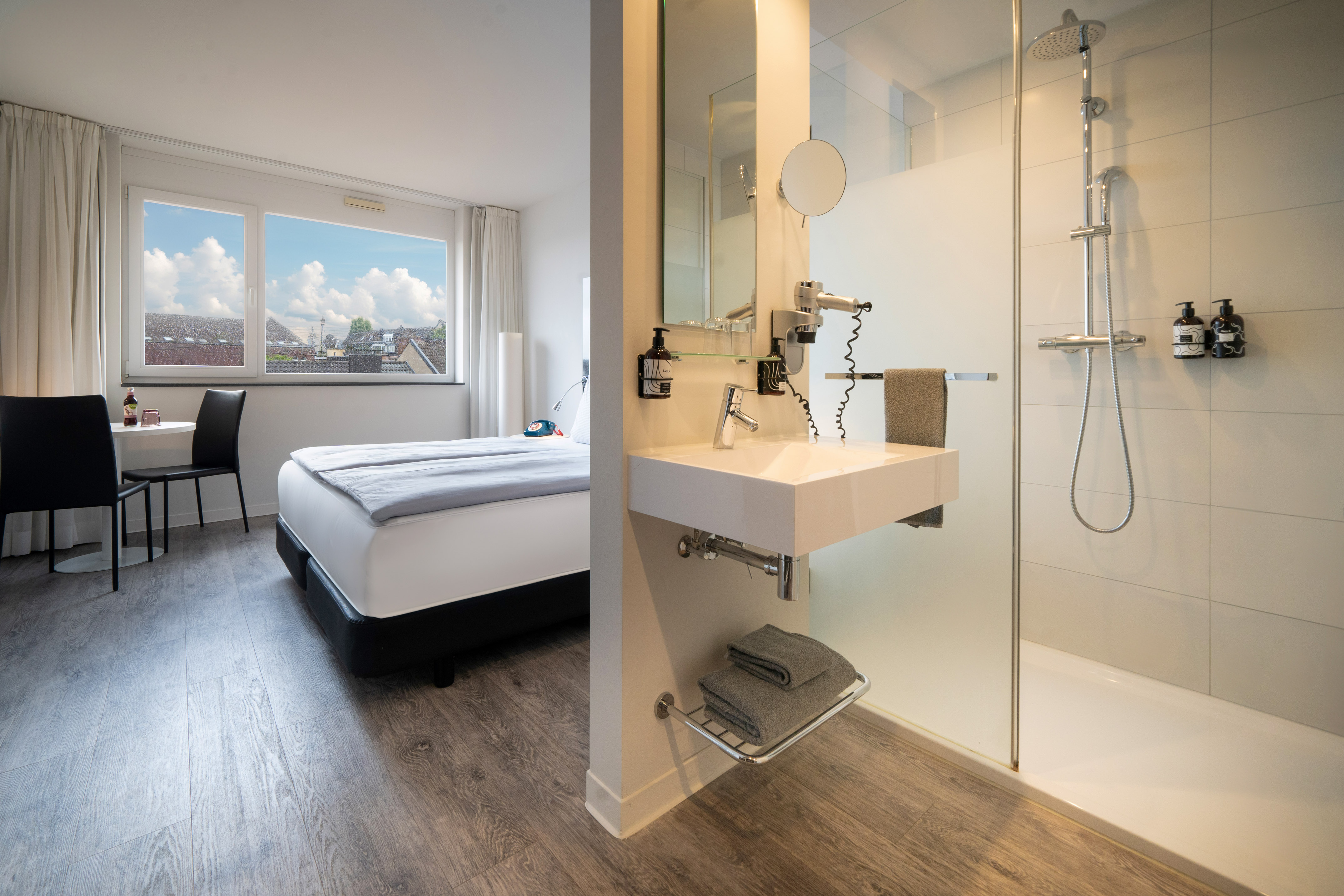 Contemporary hotel room with bed, city view, and integrated shower/sink.