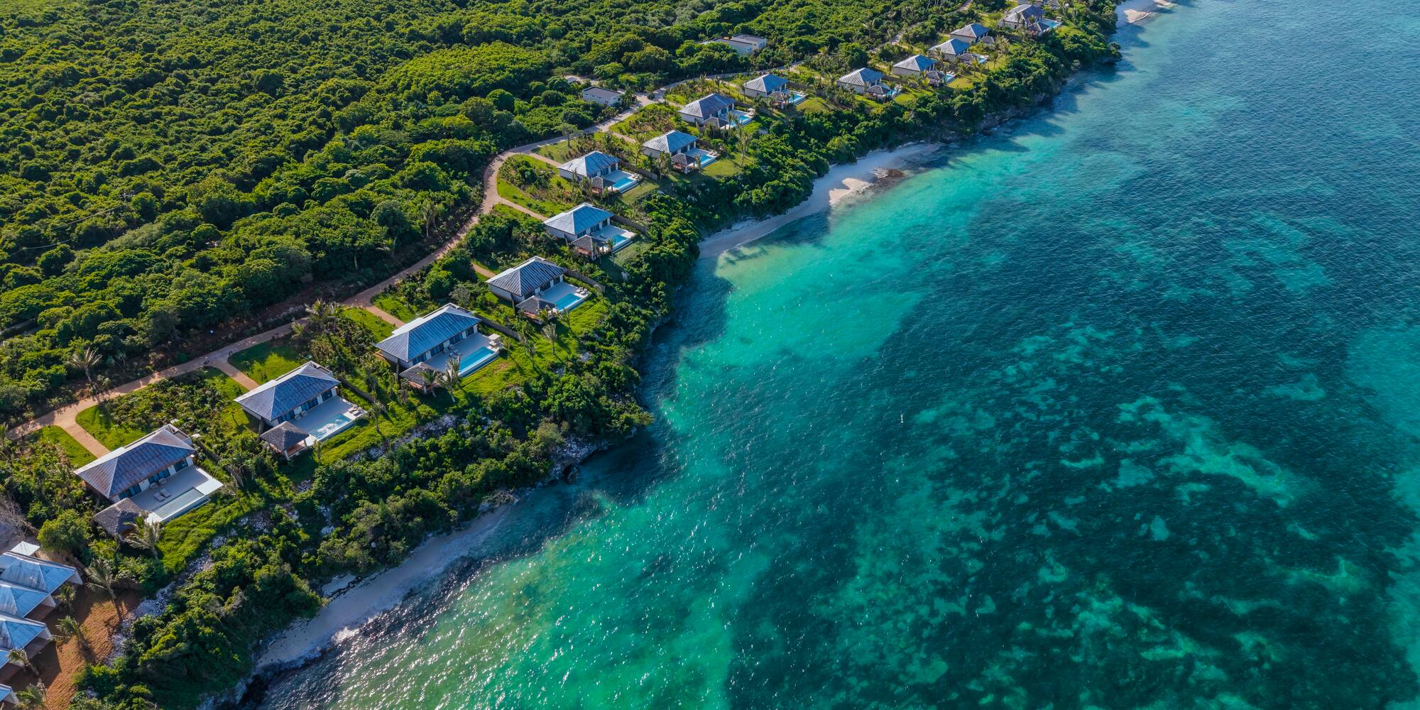Tropical coastline aerial: Luxury villas, lush forest, white sand beach, turquoise ocean.