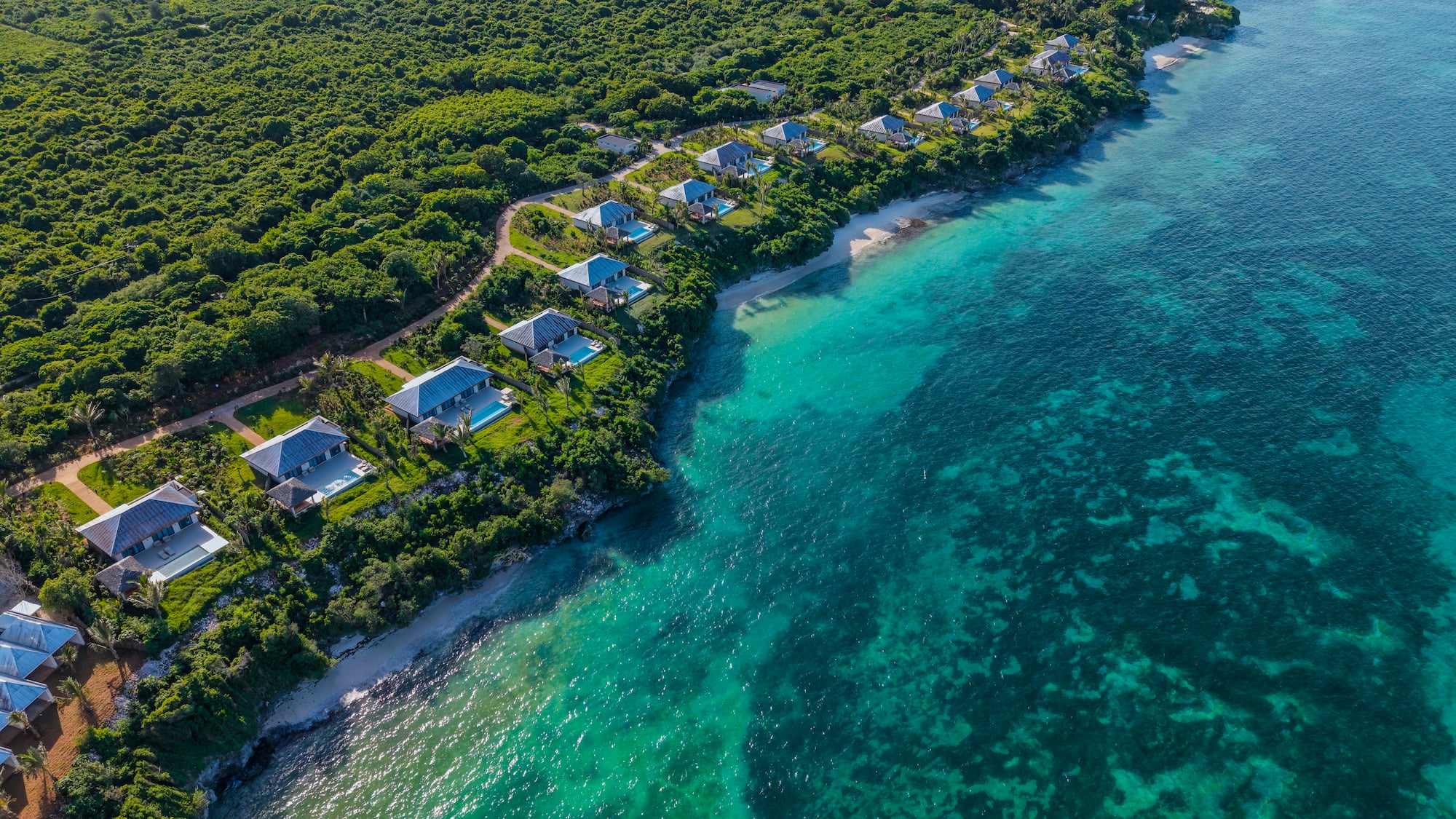 Tropical coastline aerial: Luxury villas, lush forest, white sand beach, turquoise ocean.