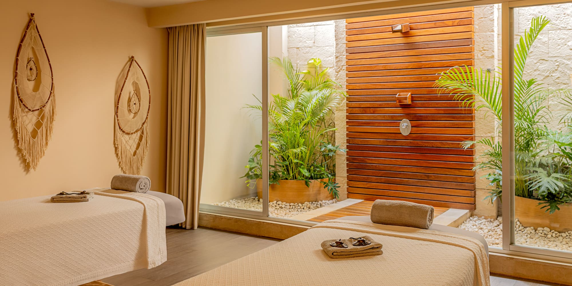 Luxury spa room with two massage tables, outdoor shower, and tropical plants.