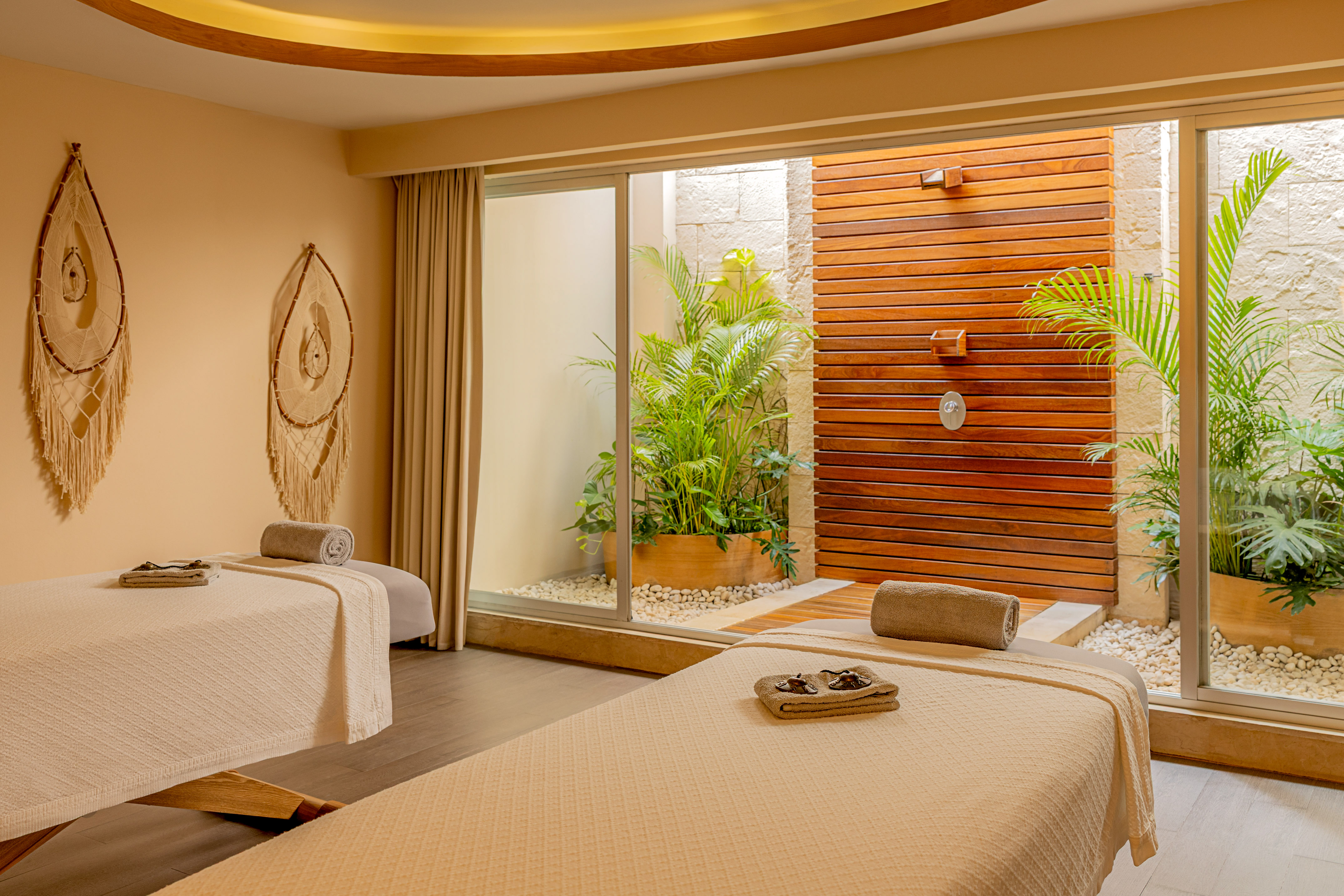Luxury spa room with two massage tables, outdoor shower, and tropical plants.