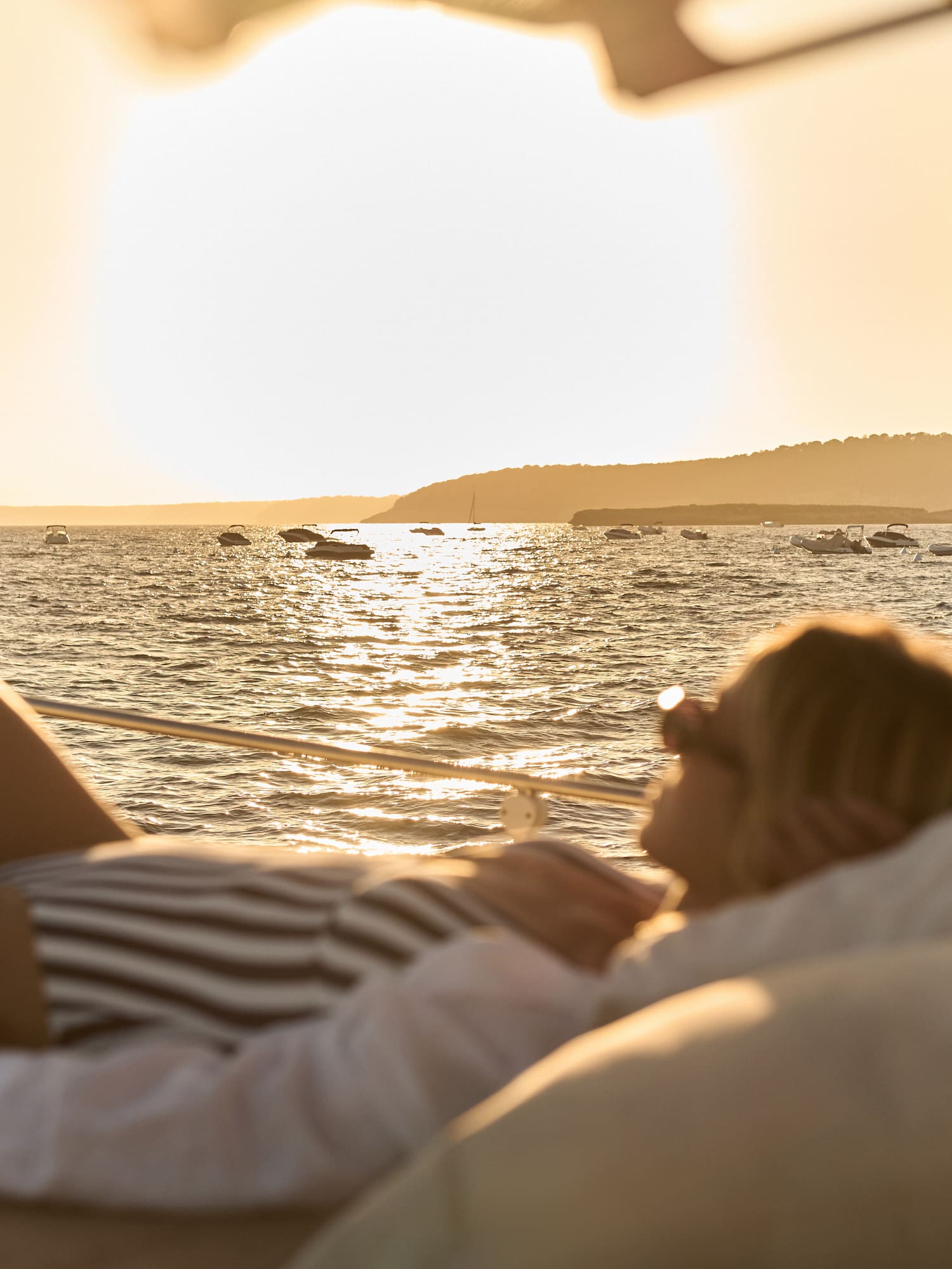 Mujer en barco, atardecer dorado en el mar con yates.