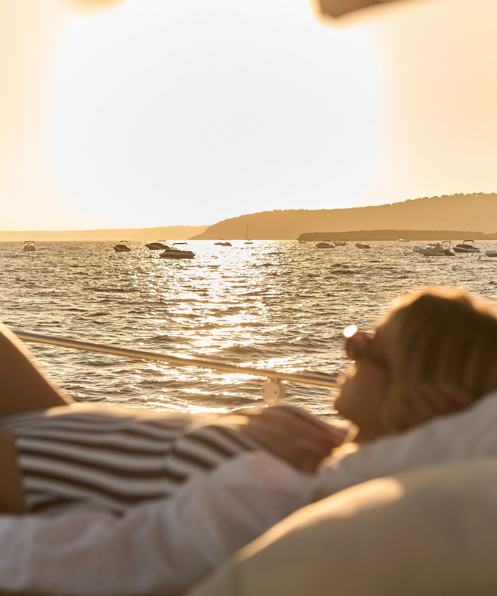 Mujer en barco, atardecer dorado en el mar con yates.