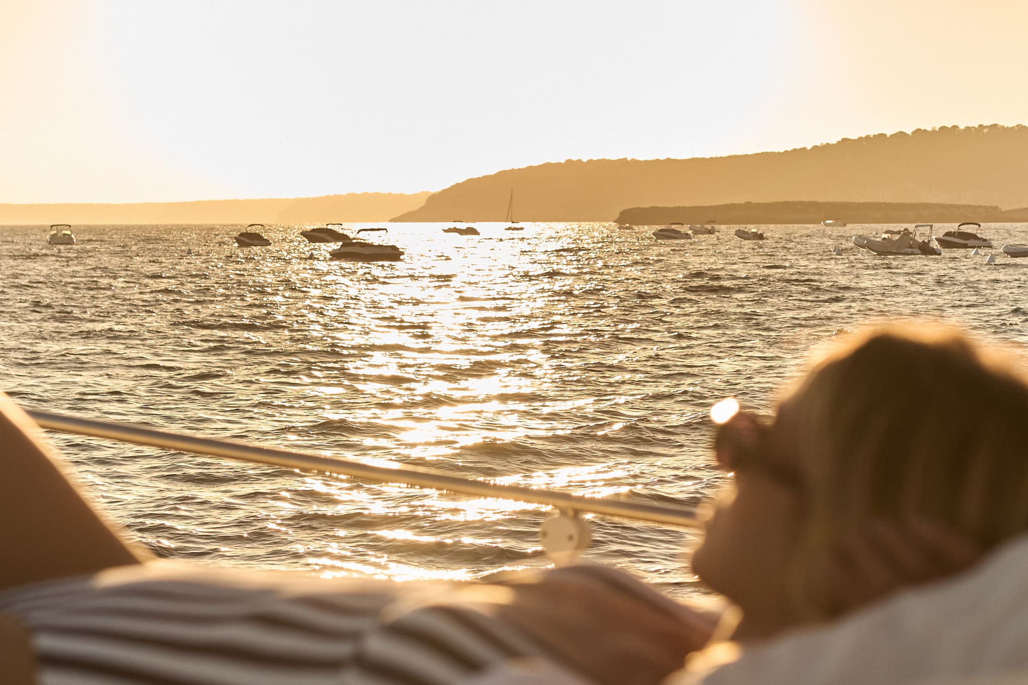 Mujer en barco, atardecer dorado en el mar con yates.