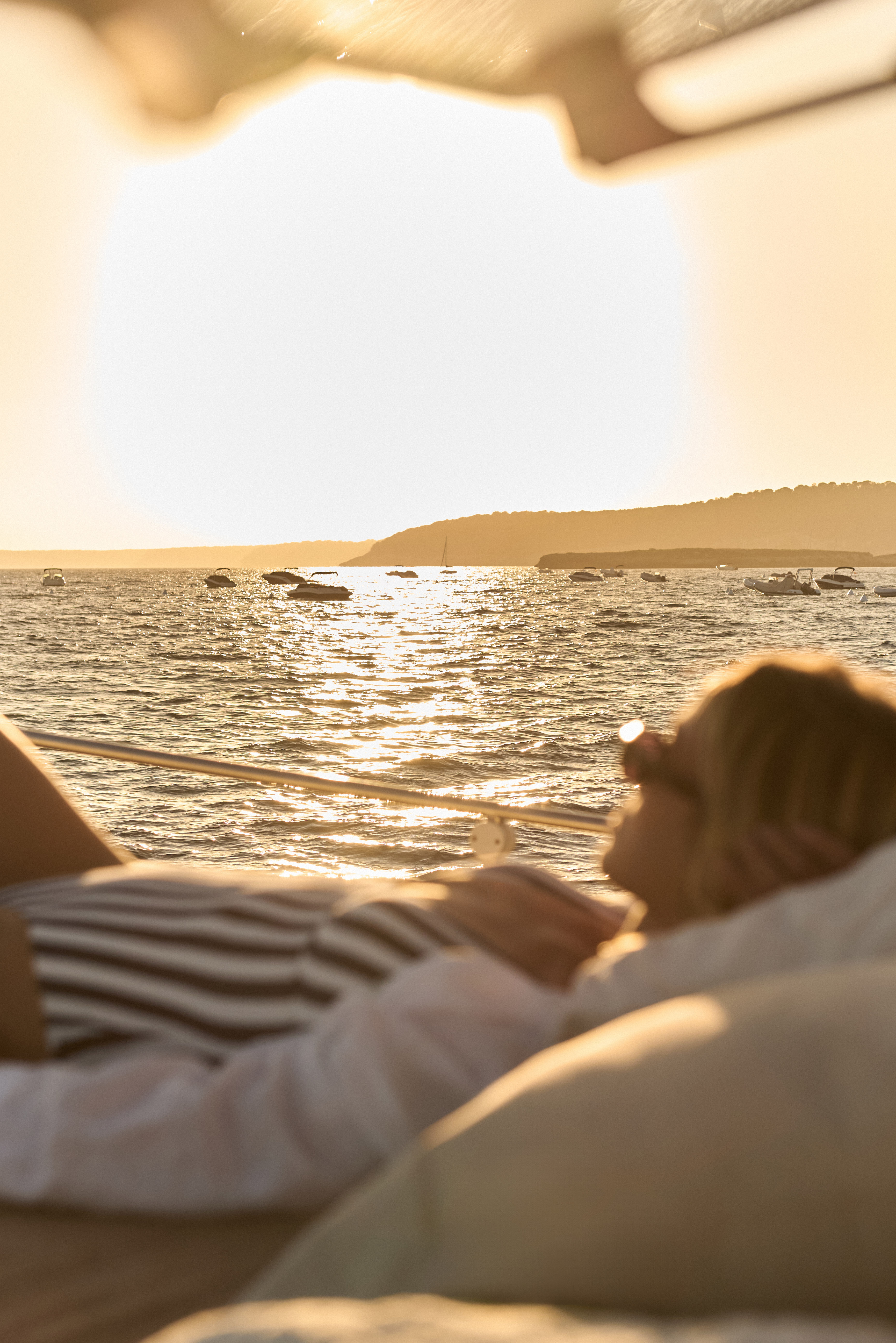 Mujer en barco, atardecer dorado en el mar con yates.