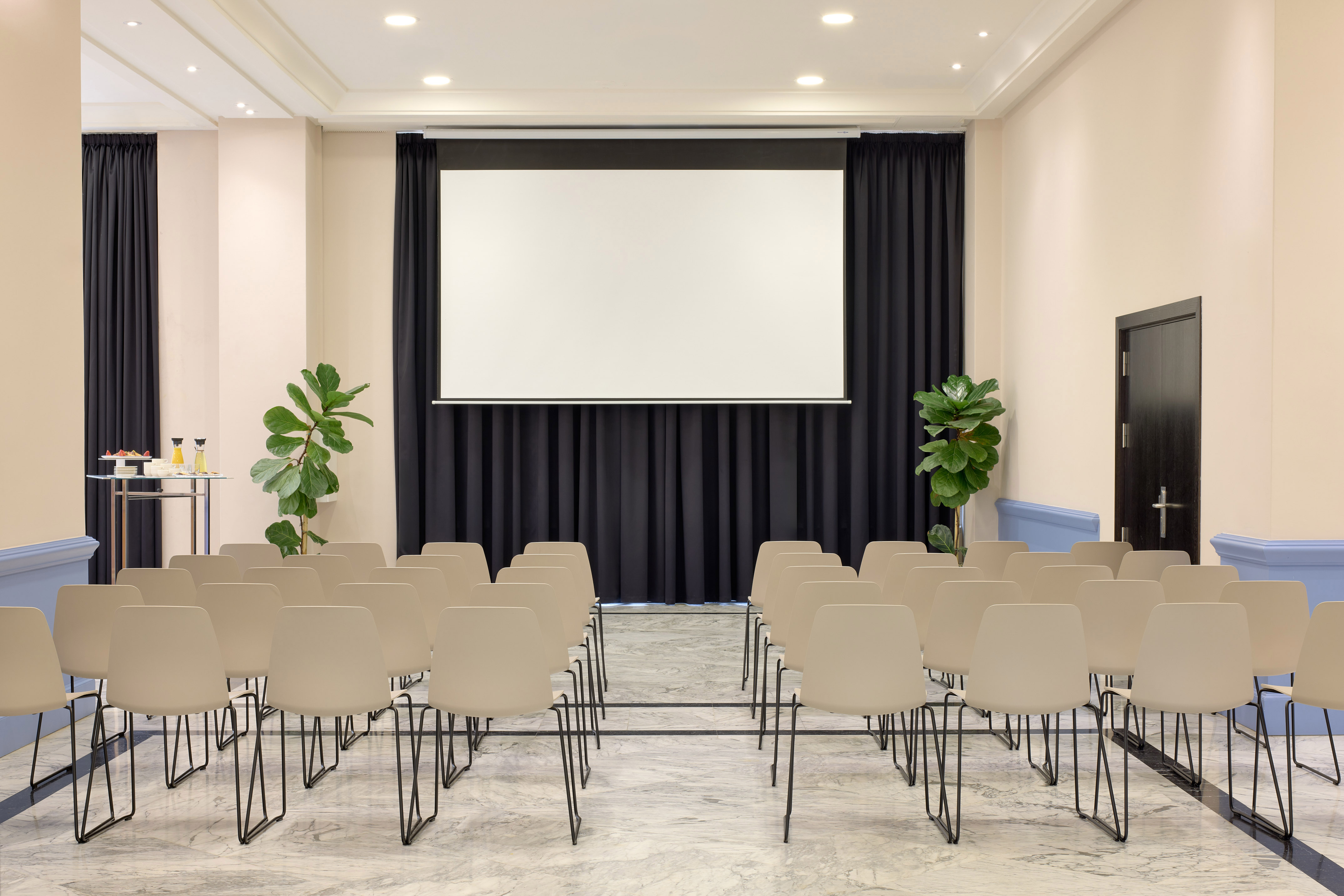 Modern empty meeting room with projector screen, beige chairs, and refreshments.