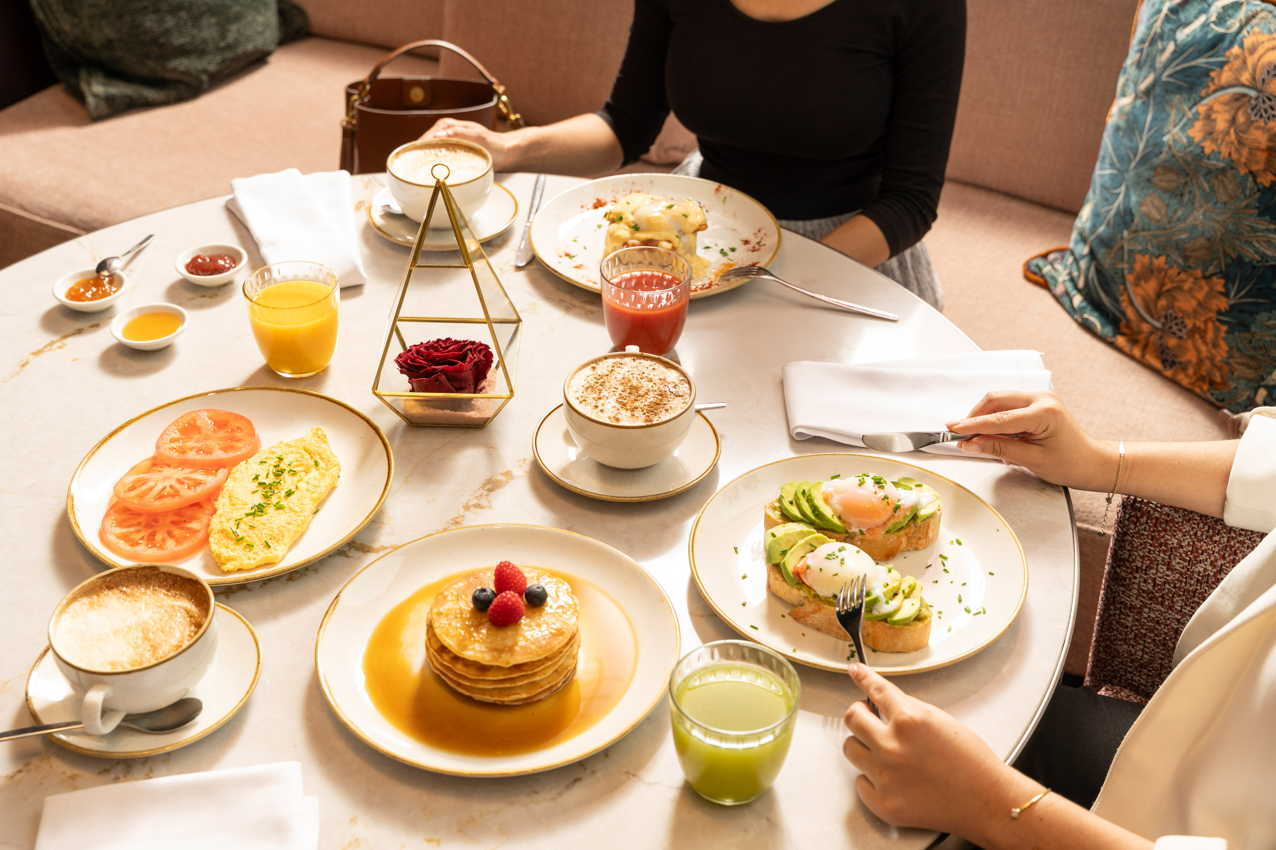 Breakfast table with pancakes, avocado toast, eggs, coffee, and juices for two people.