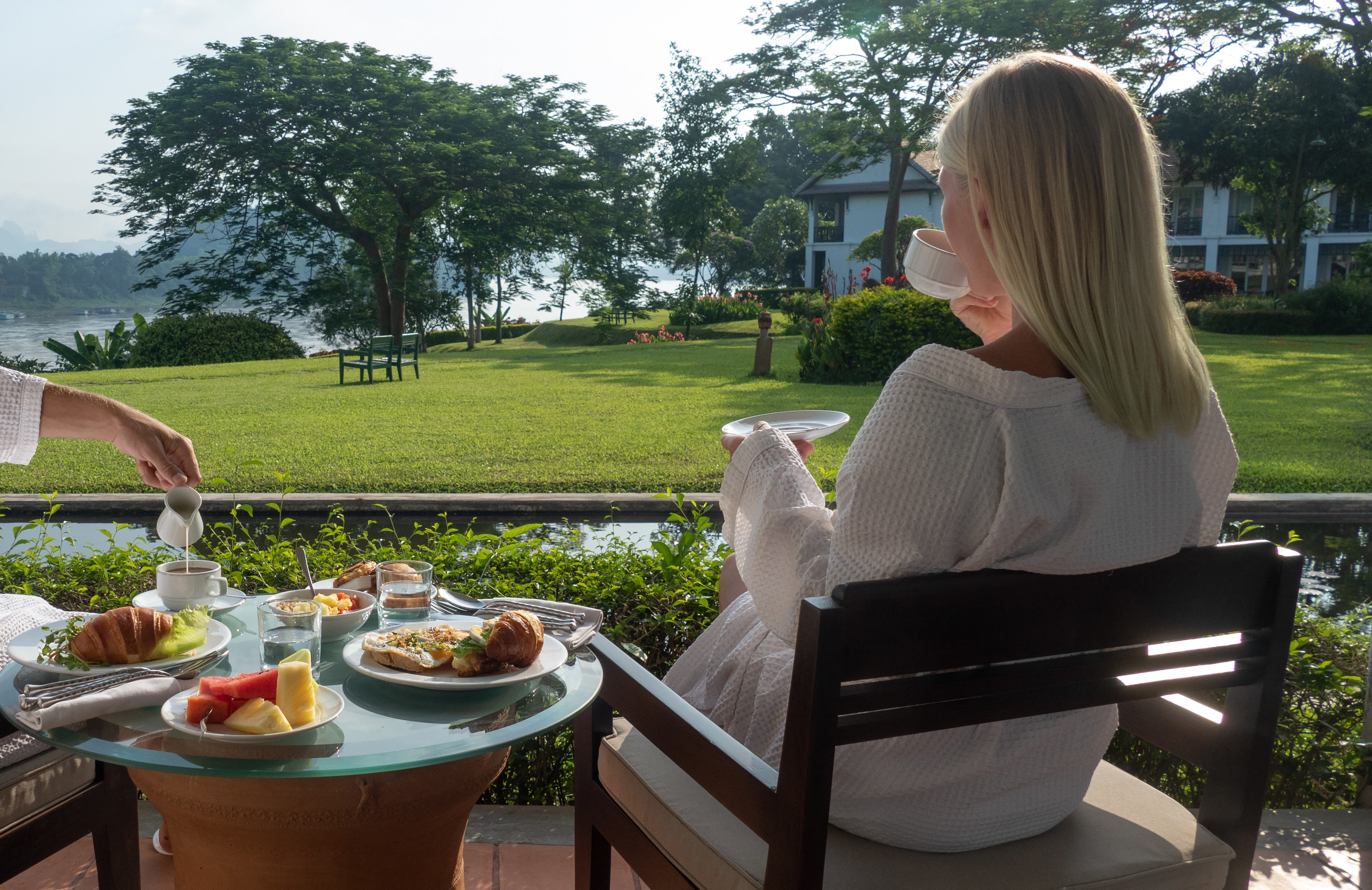 Woman enjoying outdoor breakfast at resort with scenic lake view.