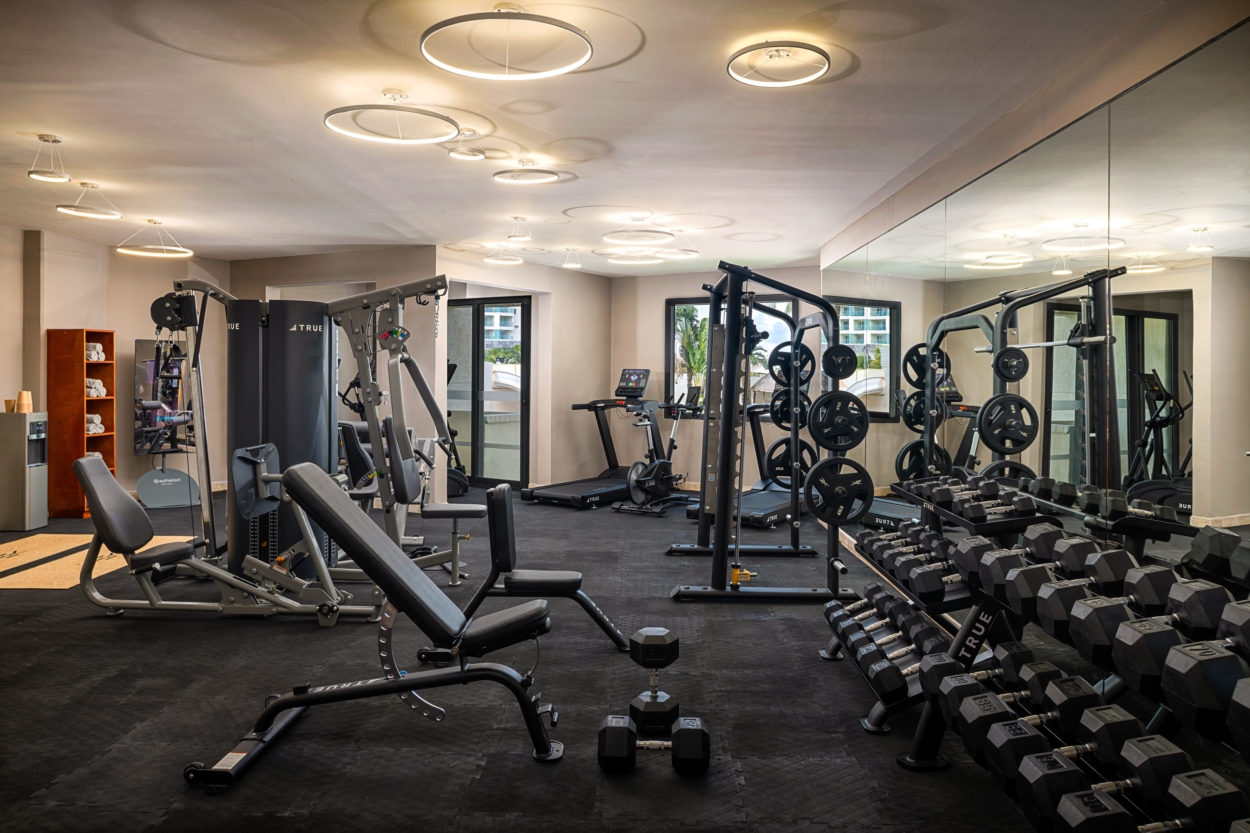Spacious gym with dumbbells, weight machines, treadmills, and bright ring lighting.