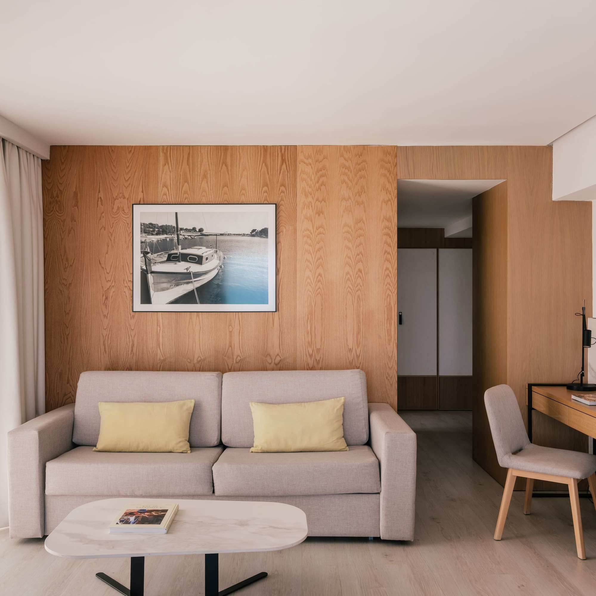 Modern hotel suite living room with sofa, wood wall, desk, and framed boat art.