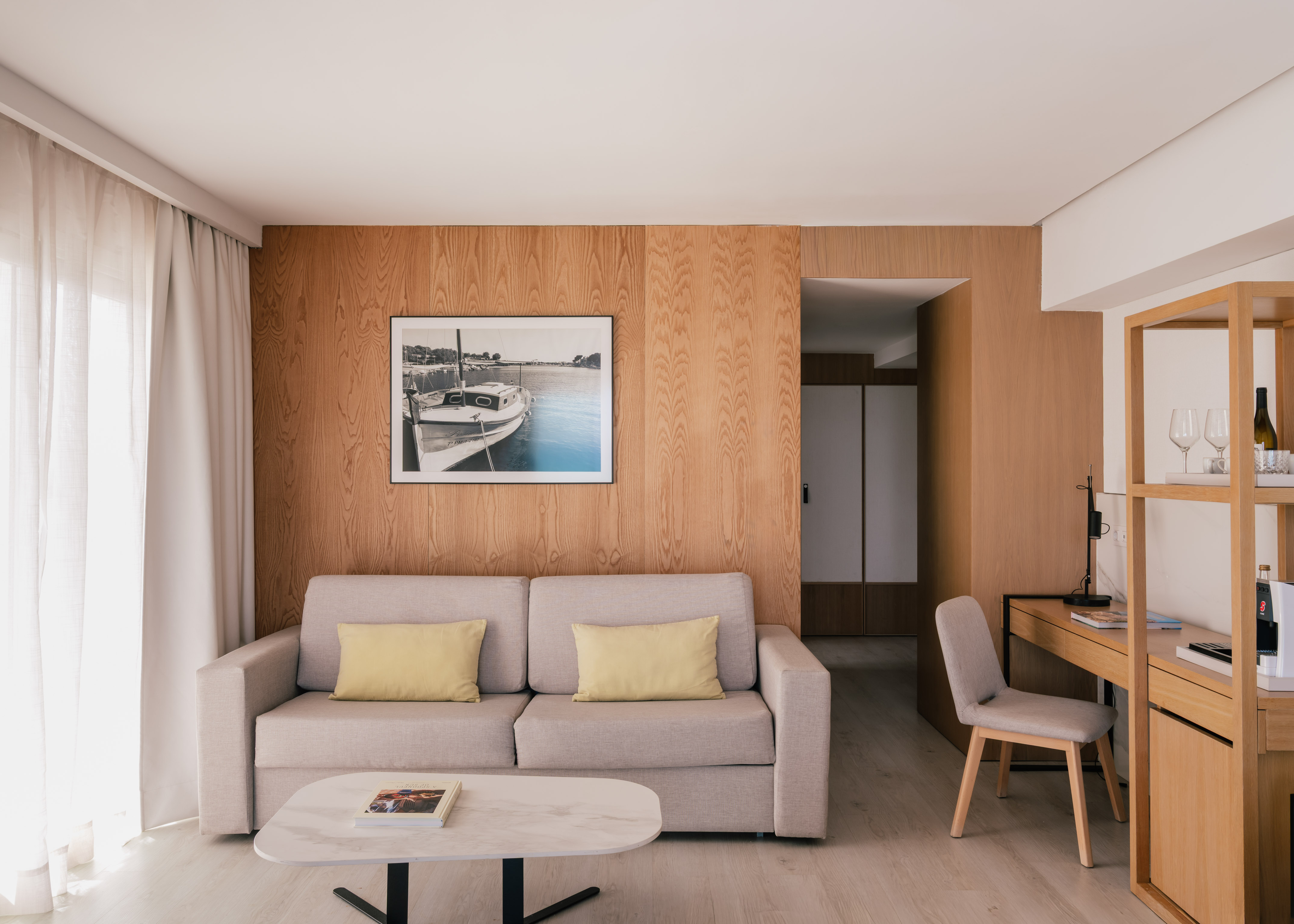 Modern hotel suite living room with sofa, wood wall, desk, and framed boat art.
